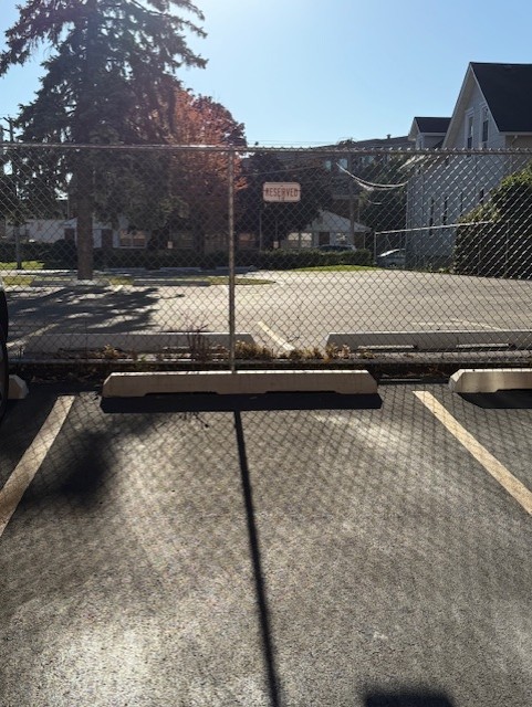 Fenced parking lot with marked spaces and a reserved sign beside a residential building.