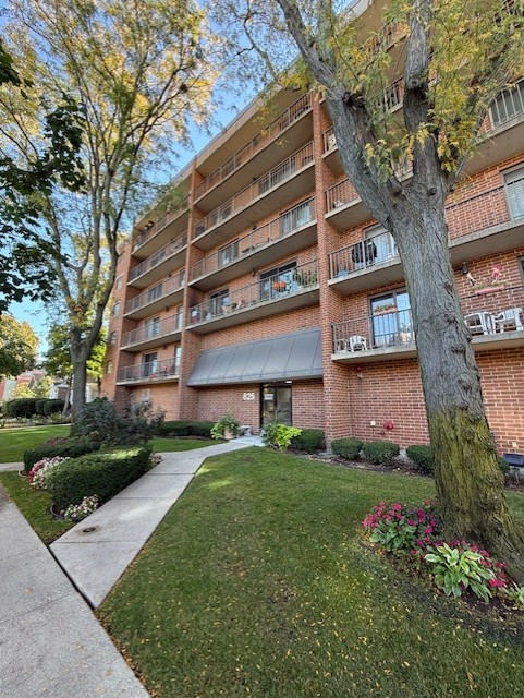 Brick condominium building with balconies, mature trees, and landscaped grounds.