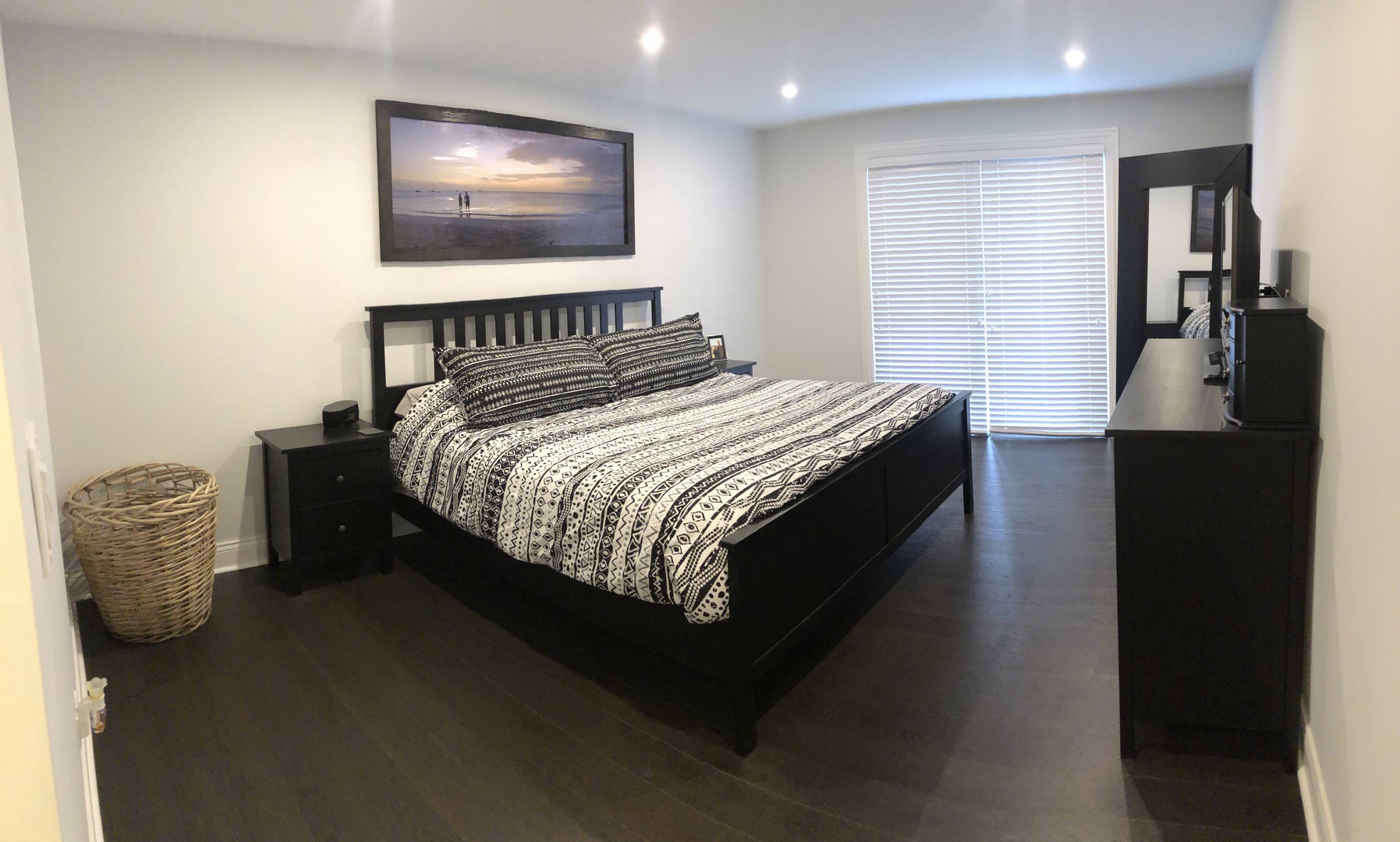 Bedroom with a black bed, patterned bedding, dark wood furniture, and a window with blinds.