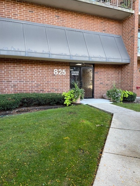 Brick building entrance at 825, with a gray awning, landscaped lawn, and walkway.