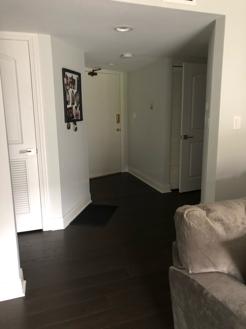 Entry hall with dark wood floors, a white front door, and a framed photo display.