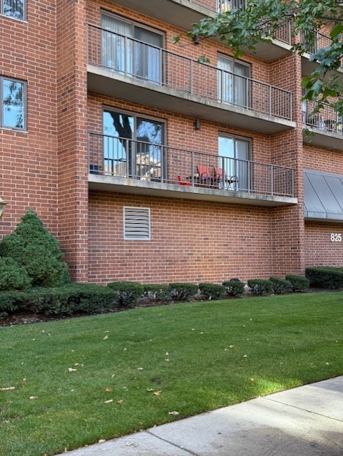 Red-brick apartment building with metal-railed balconies and a landscaped lawn.