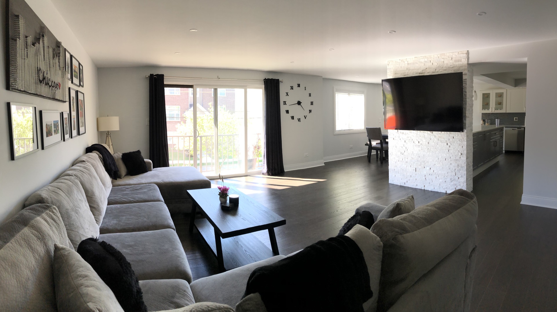 Furnished living room with gray sectional sofas, balcony doors, and a stone television partition.