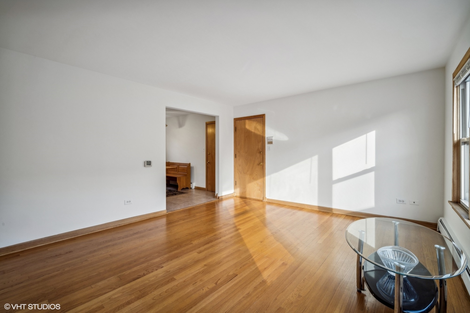 Living room with hardwood floors, a large window, and a glass coffee table.