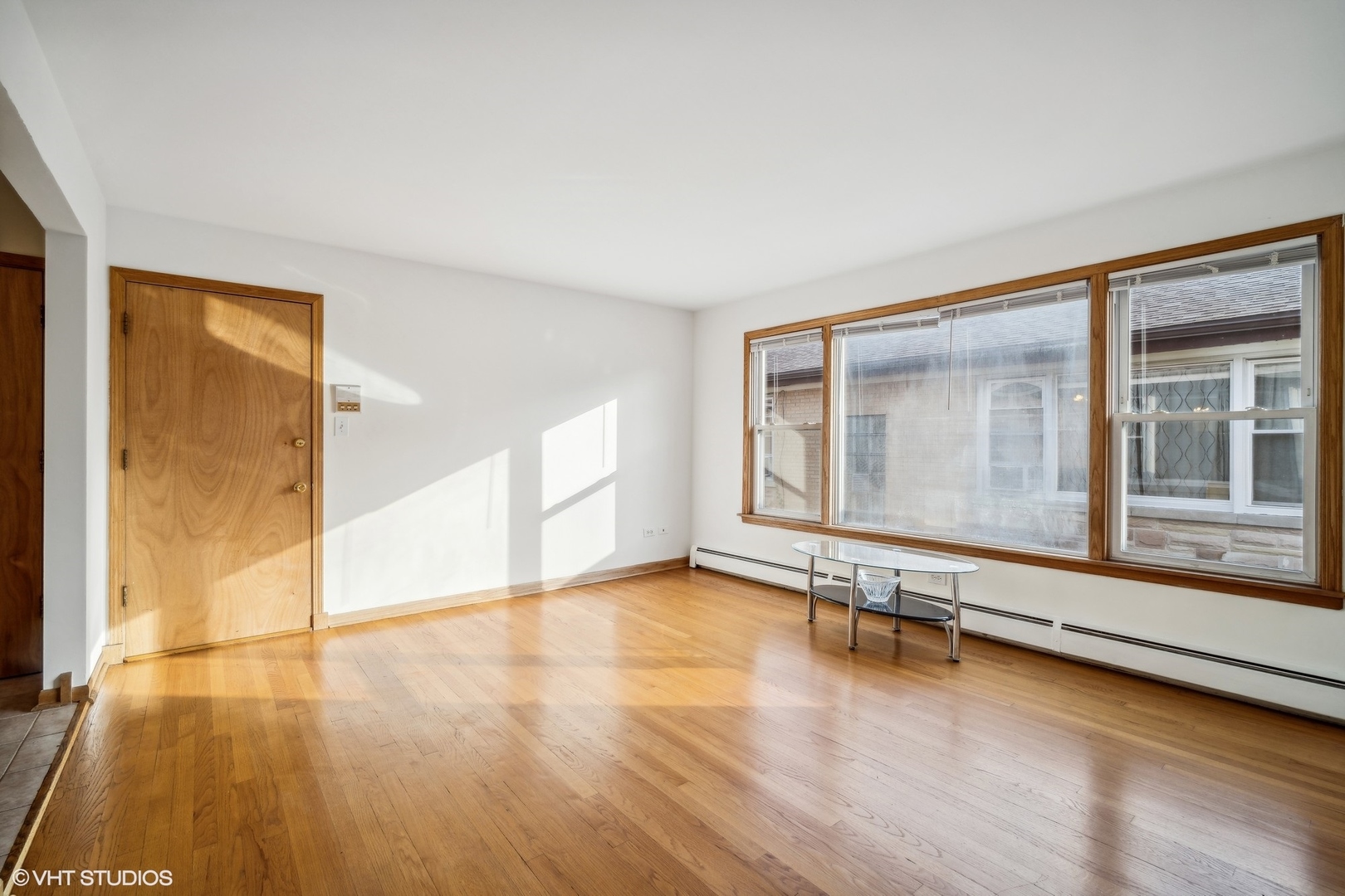 Living room with hardwood floors, large wood-trimmed windows, and a small glass coffee table.