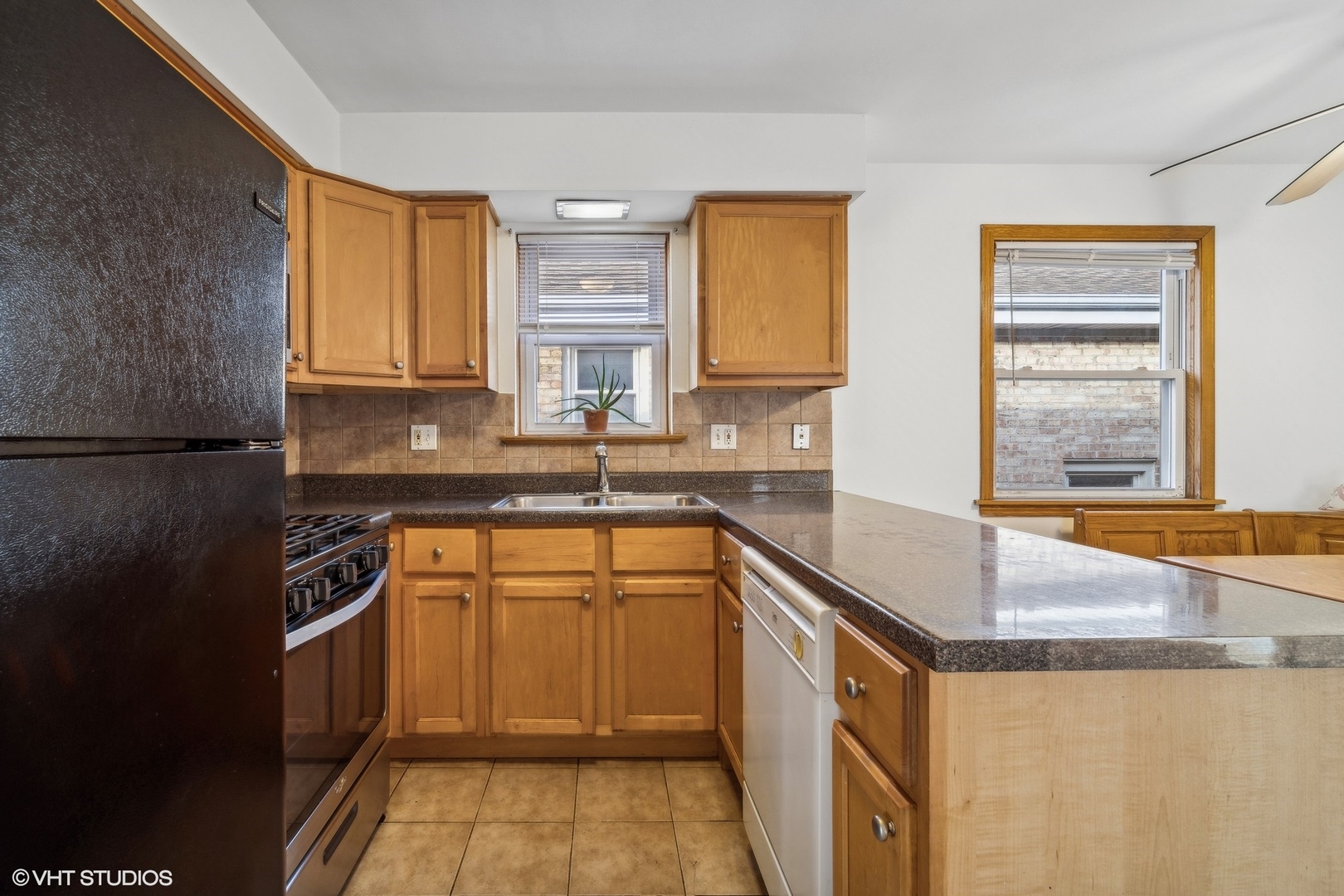 Kitchen with honey-toned cabinets, dark counters, a long peninsula, and two windows.