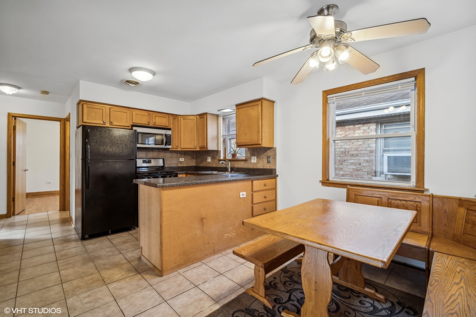Kitchen with honey-colored cabinets, black appliances, and a wood dining table beside a large window.