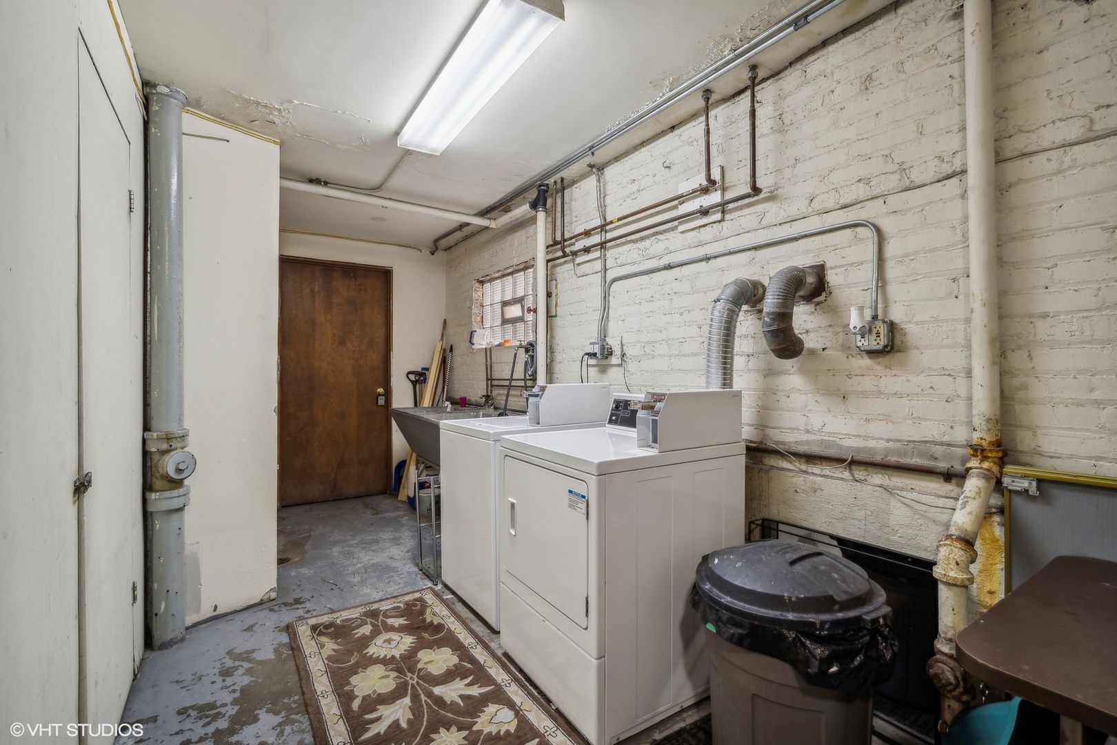Basement laundry room with washer and dryer, utility sink, and exposed brick walls.