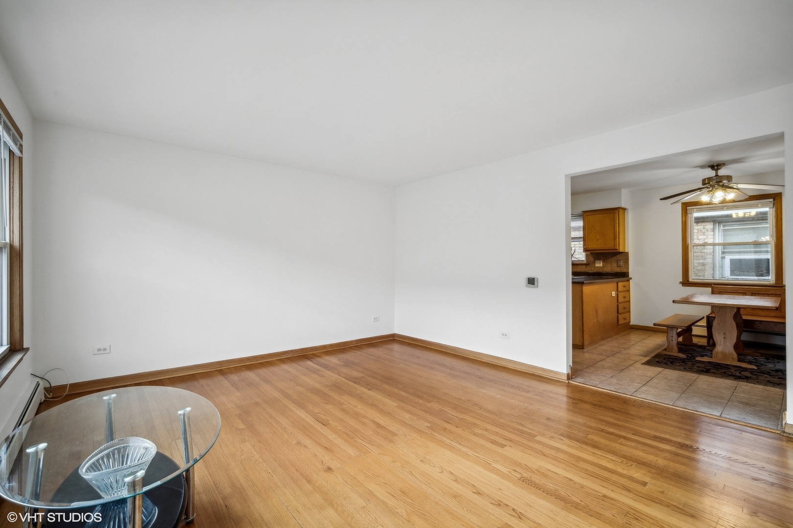 Living room with hardwood floors and a glass table, opening into a tiled dining area and kitchen.