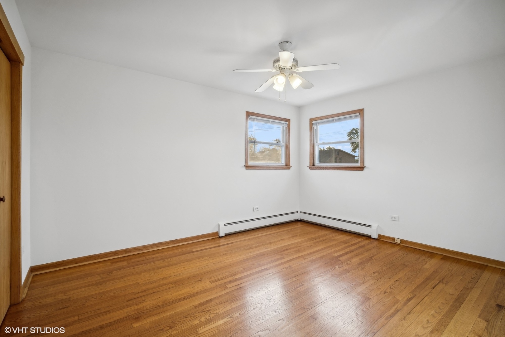 Vacant room with hardwood floors, two windows, and a ceiling fan.