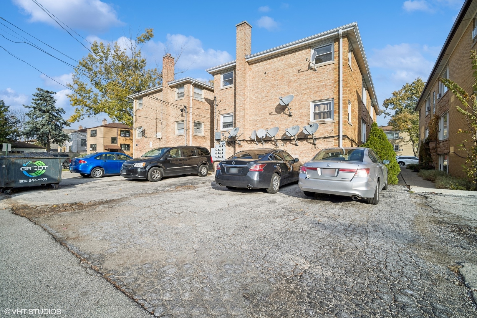 Brick apartment building beside a cracked parking lot with several parked cars.