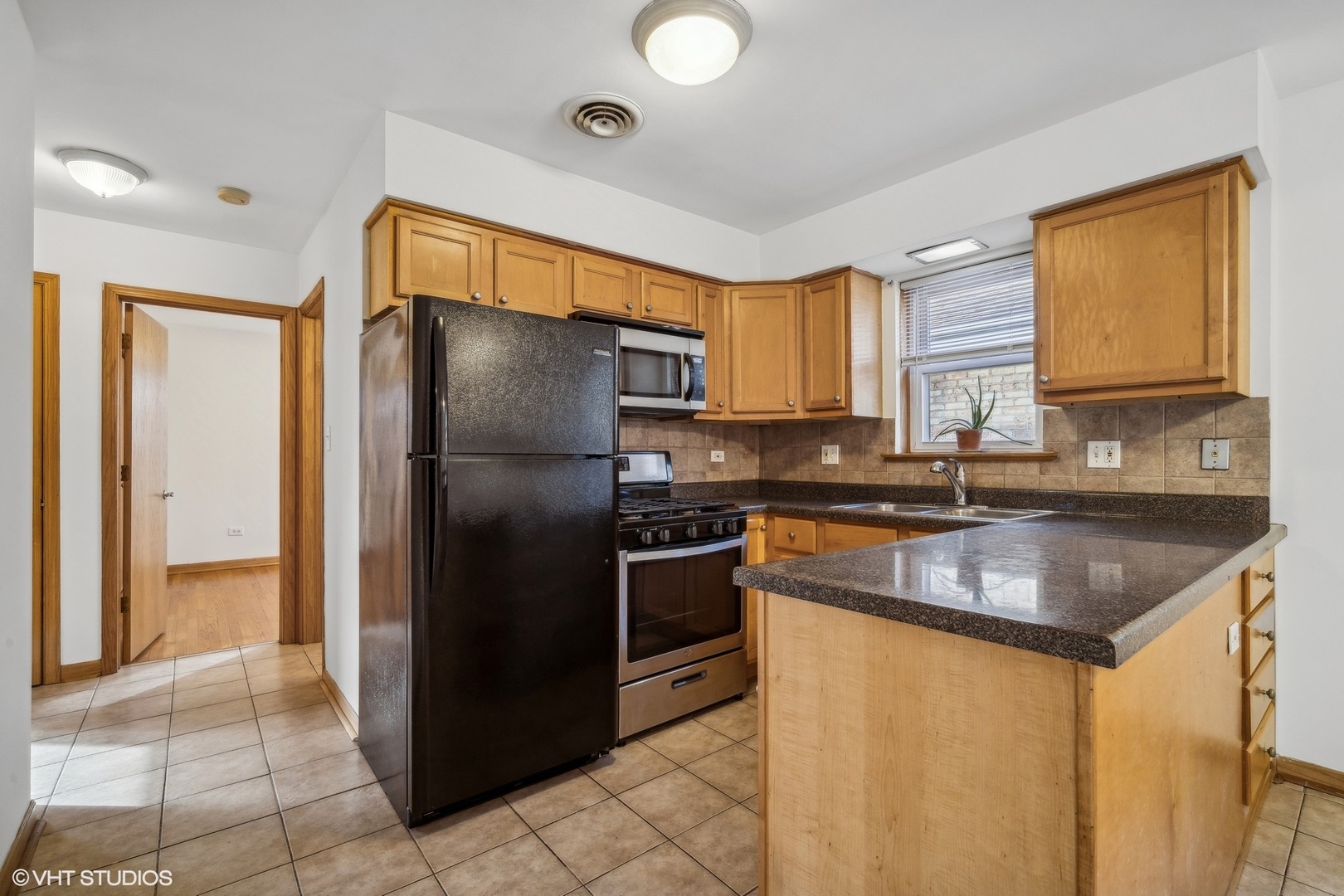 Kitchen with wood cabinets, dark granite counters, a peninsula, and black appliances.