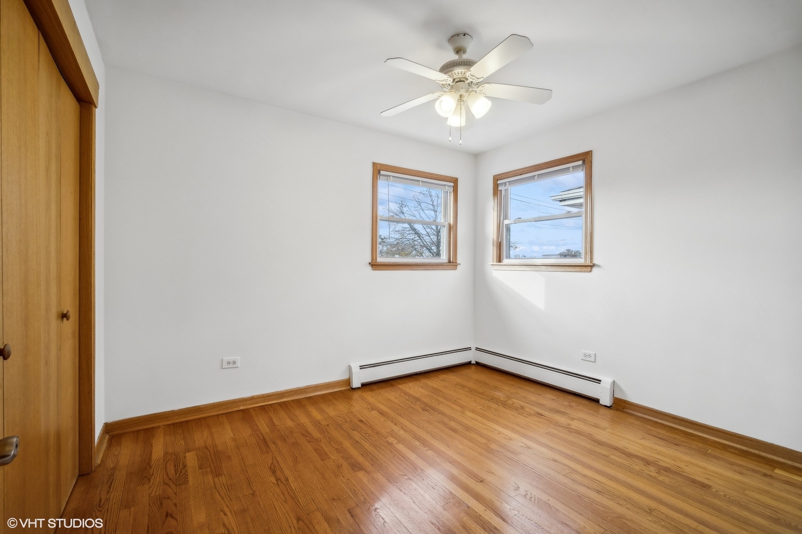 Empty bedroom with hardwood floors, two windows, and a ceiling fan.