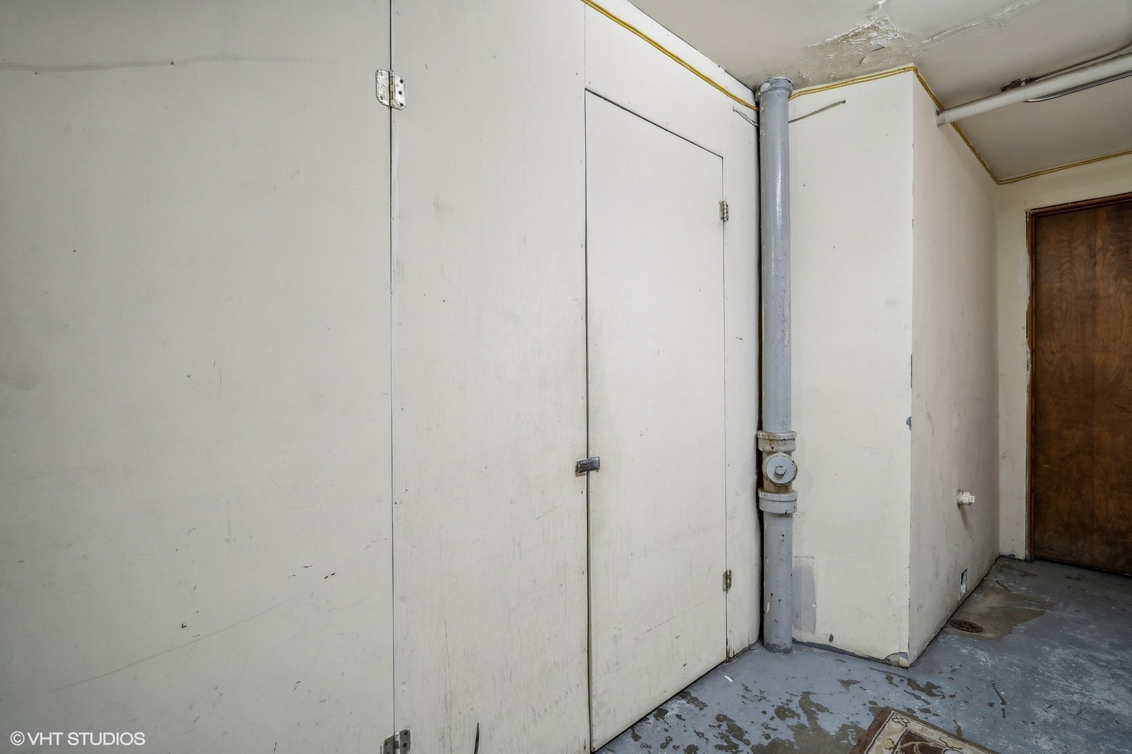 Utility area with large white storage doors, an exposed pipe, and a worn concrete floor.