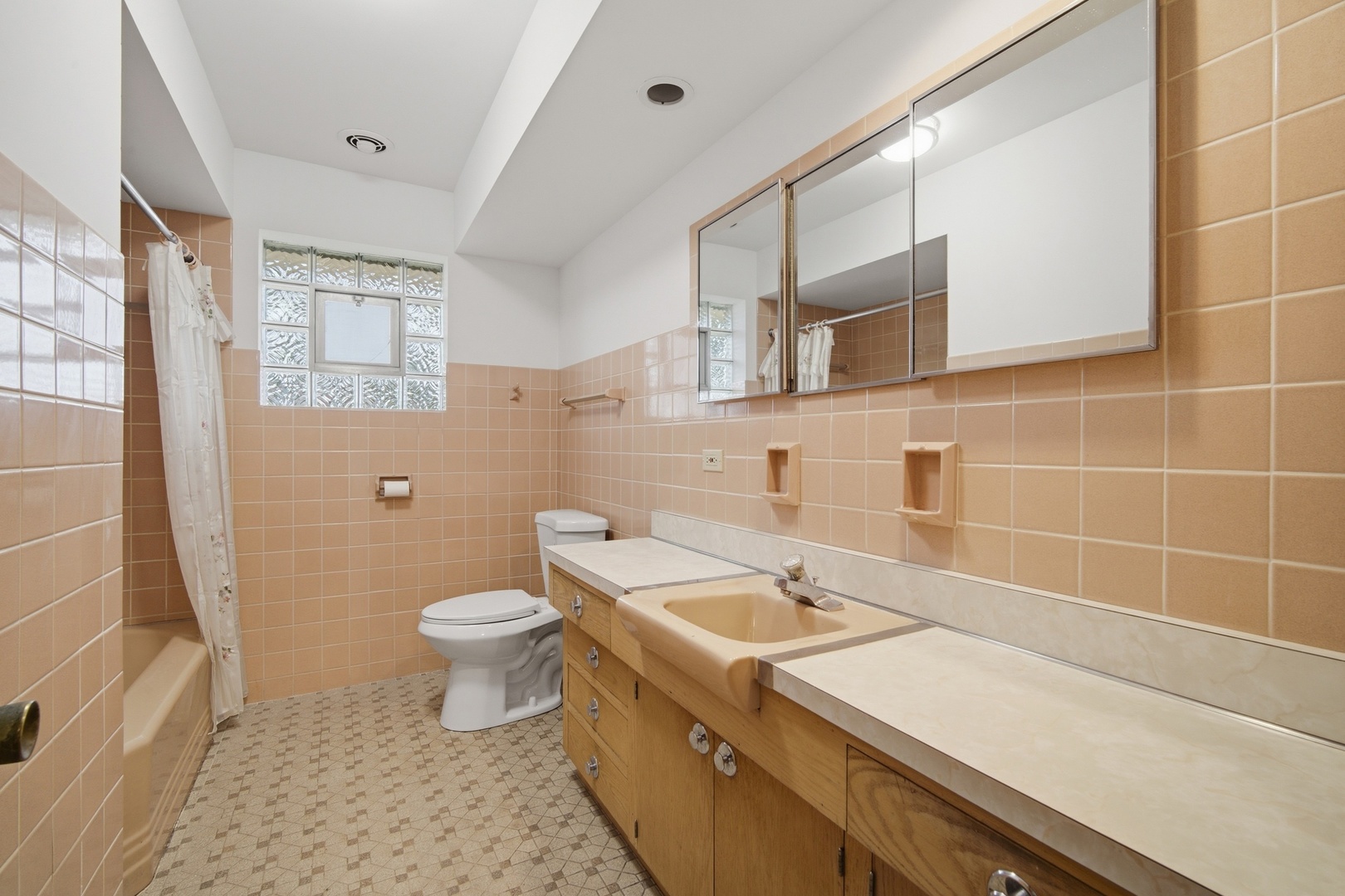 Bathroom with peach tile, a long wood vanity, mirrored cabinets, and a tub behind a shower curtain.
