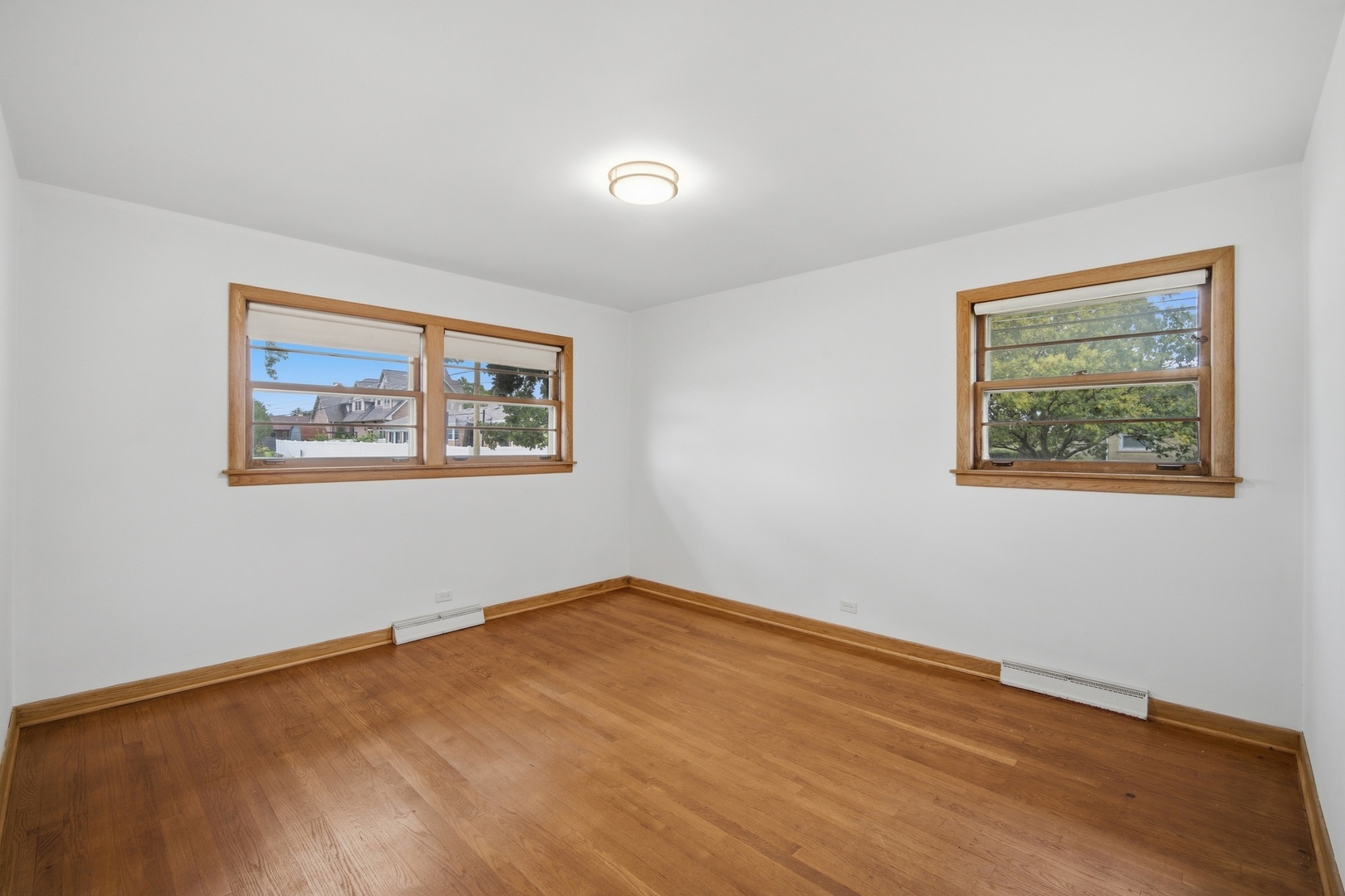Empty room with hardwood floors, wood-trimmed windows, and baseboard heaters.