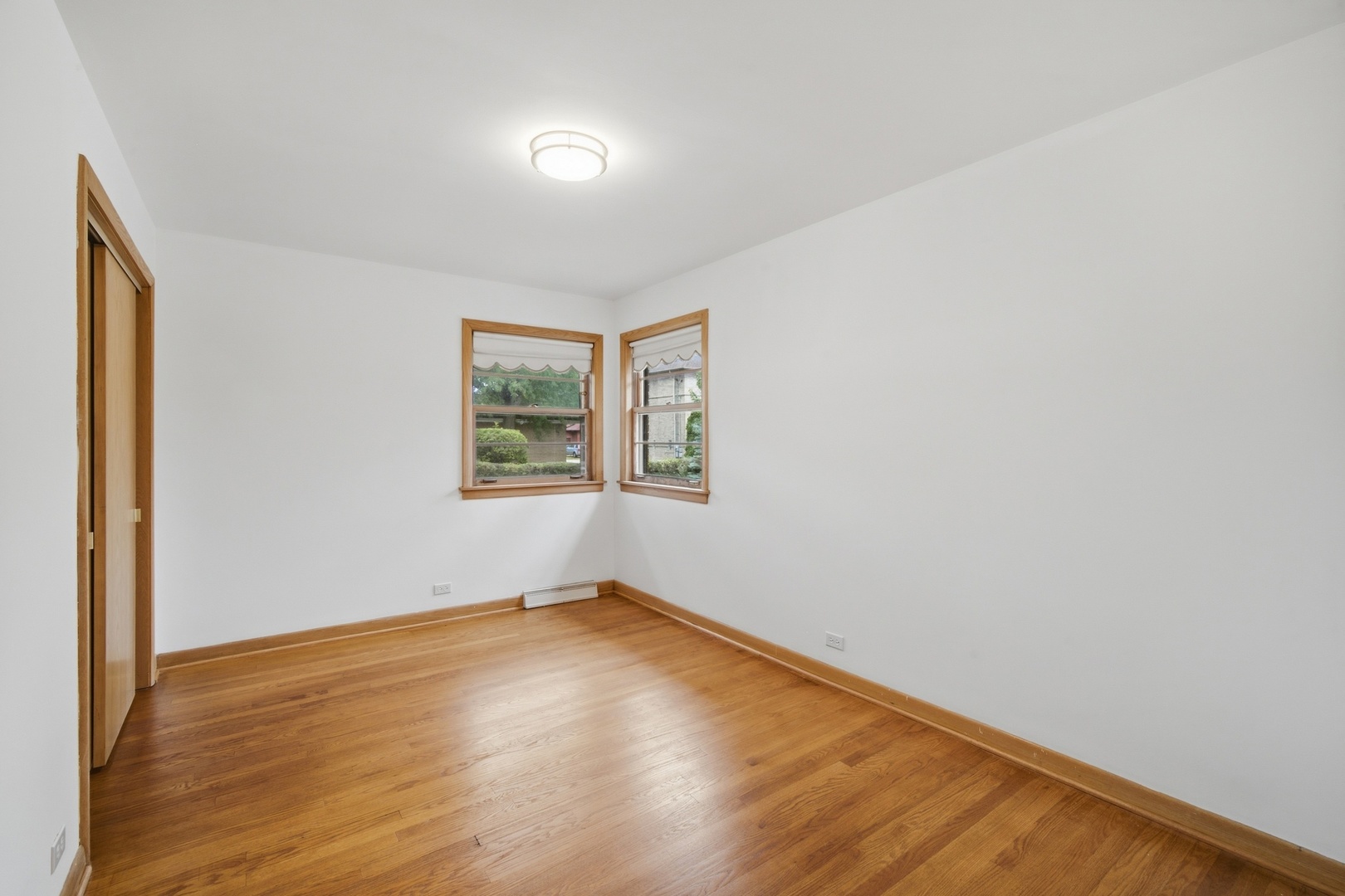 Empty room with hardwood floors, natural wood trim, and two corner windows.