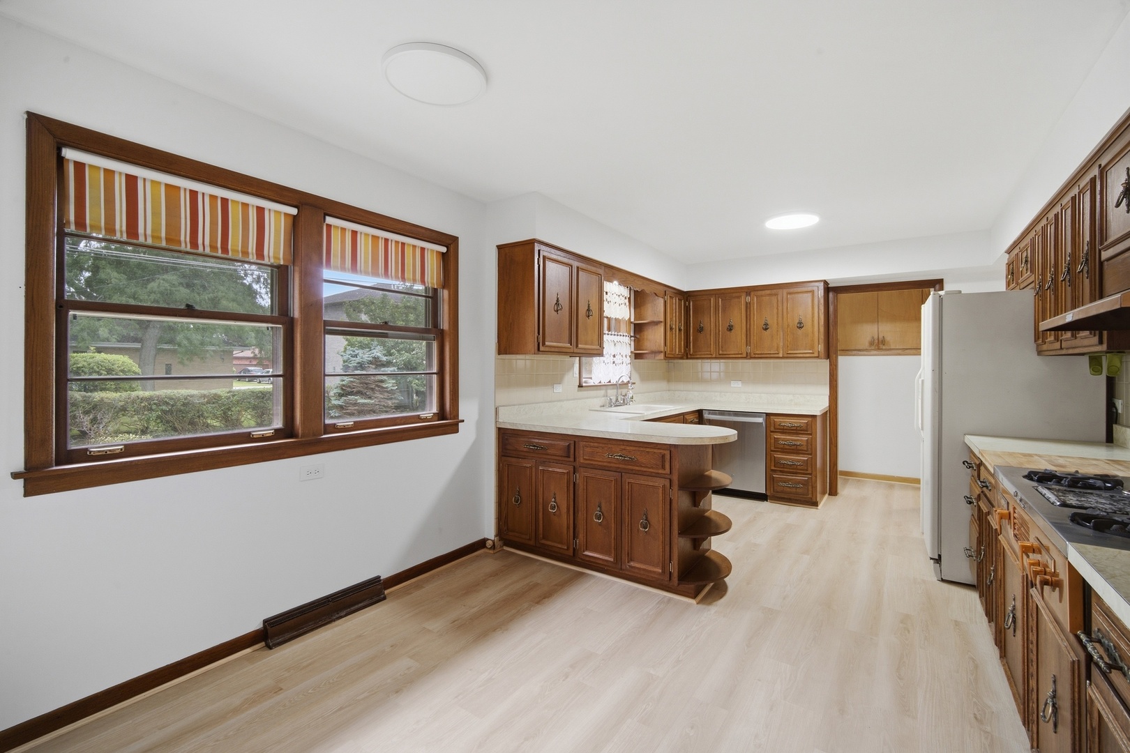 Kitchen with dark wood cabinets, a central peninsula, and two large windows with striped shades.