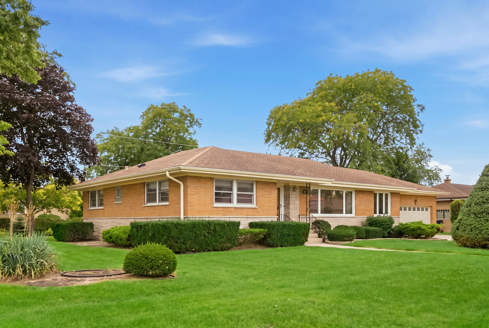 Single-story brick home with an attached garage, trimmed shrubs, and a broad front lawn.