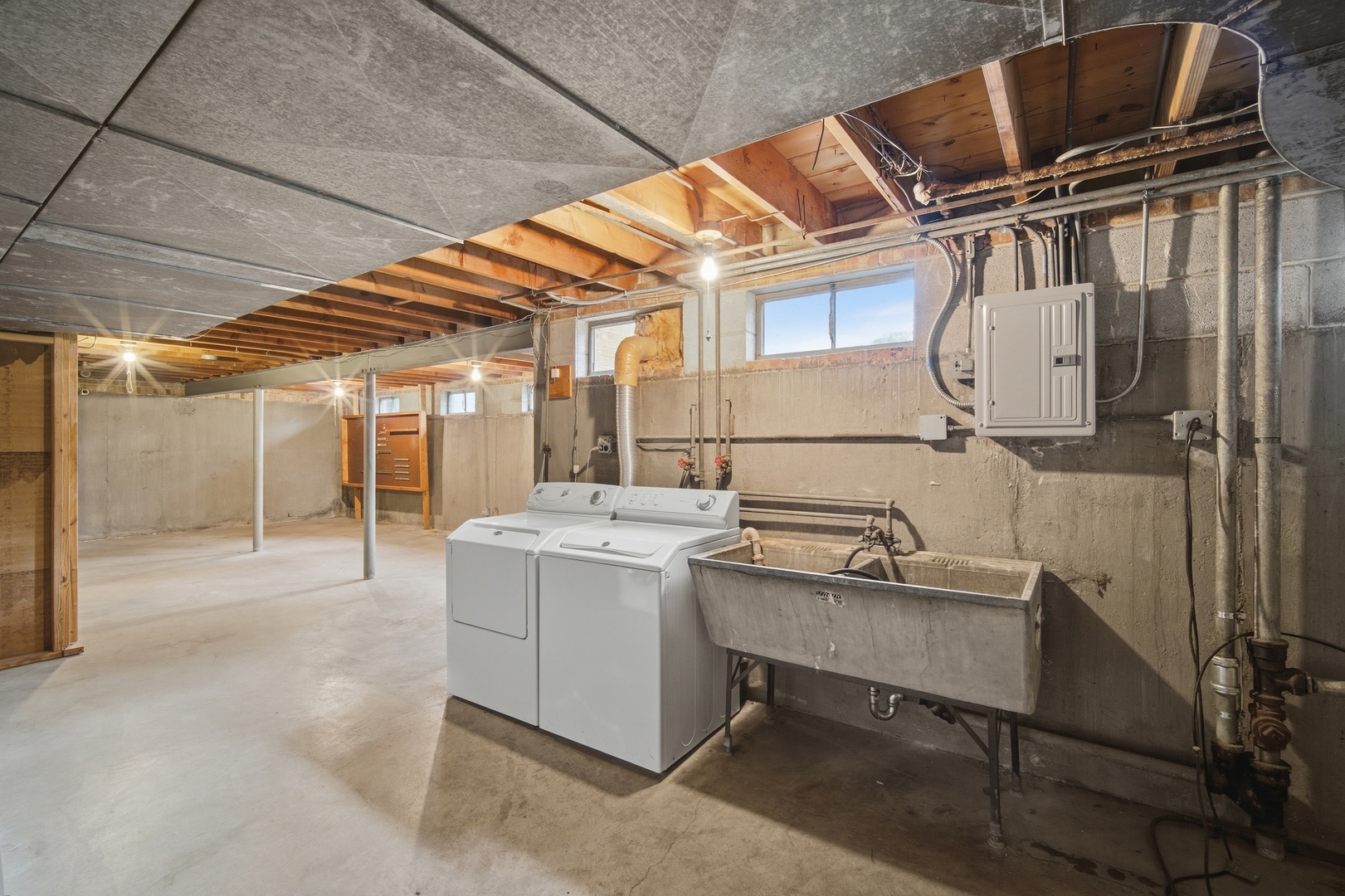 Unfinished basement laundry area with washer, dryer, and large utility sink.