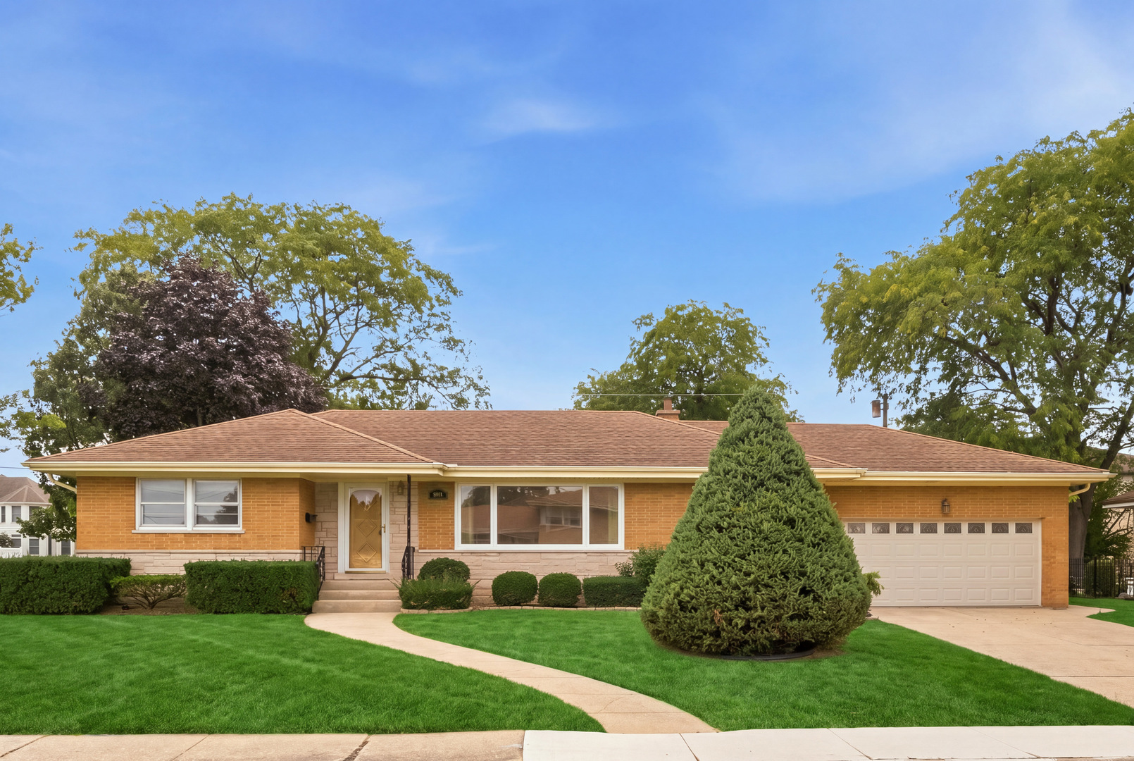 Single-story brick ranch with an attached garage, curved walkway, and large evergreen in the front lawn.
