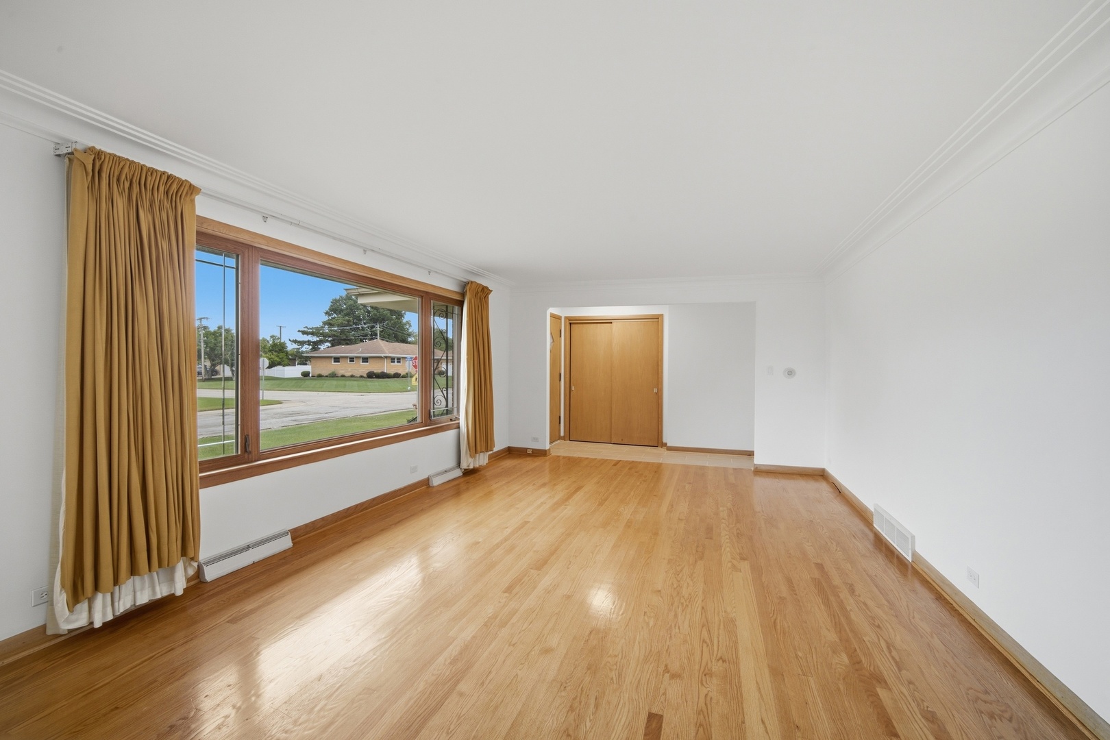 Empty room with hardwood floors, crown molding, and a large window with gold curtains.