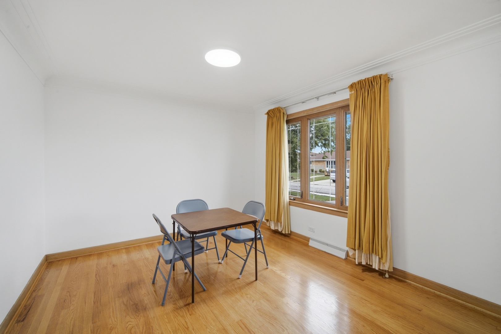 Dining room with hardwood floors, a small table, folding chairs, and mustard-yellow curtains.