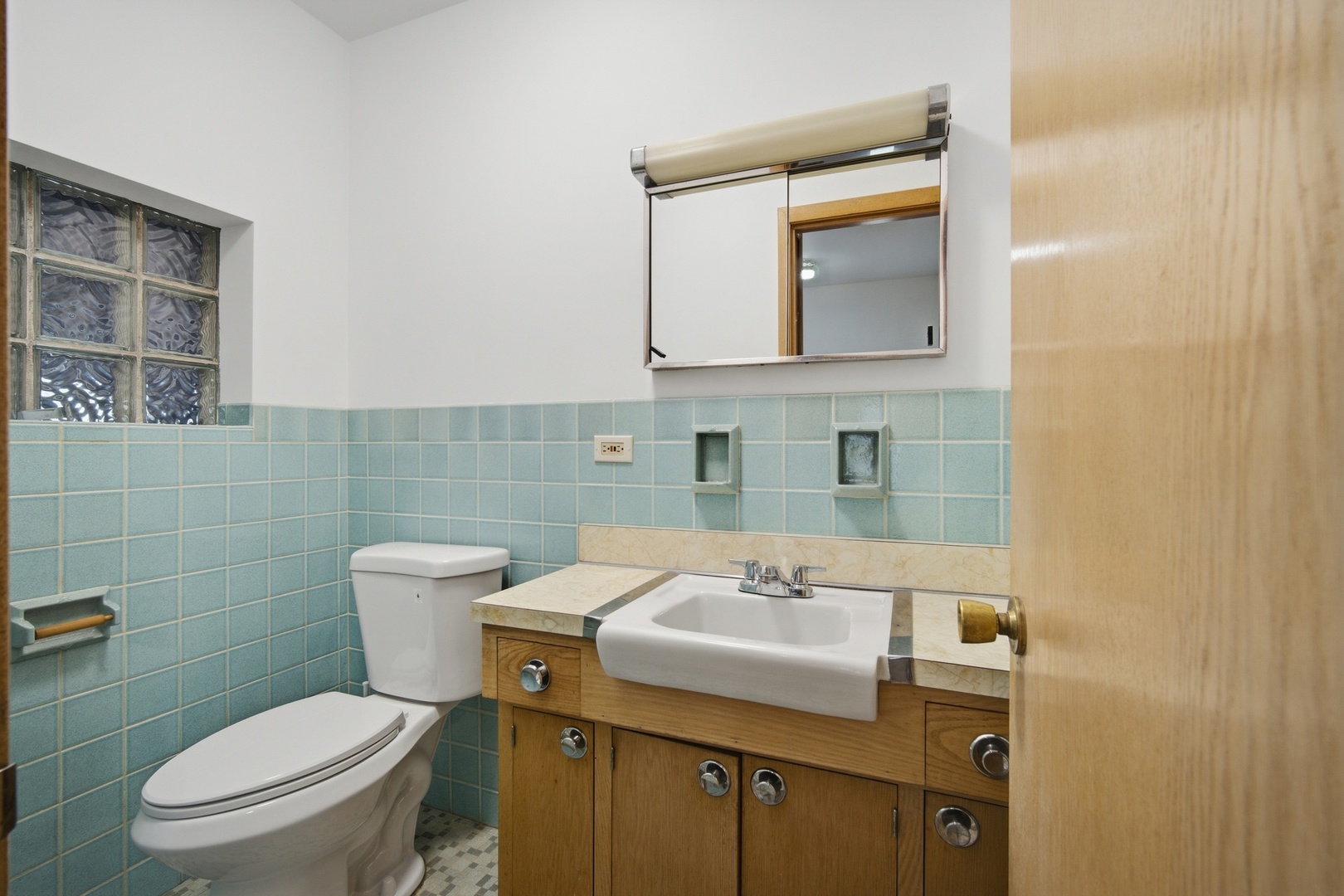 Bathroom with pale blue tile, glass-block window, and wood vanity with a large sink.