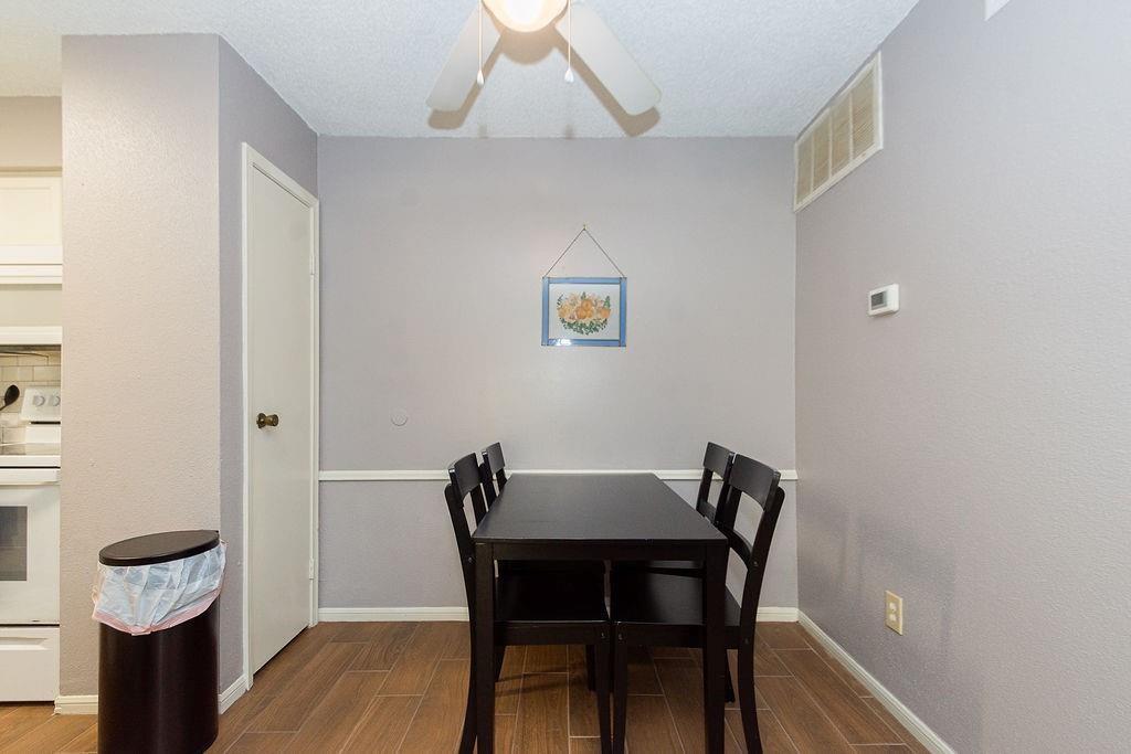 Dining area with a dark table and chairs, gray walls, wood-look flooring, and a ceiling fan.