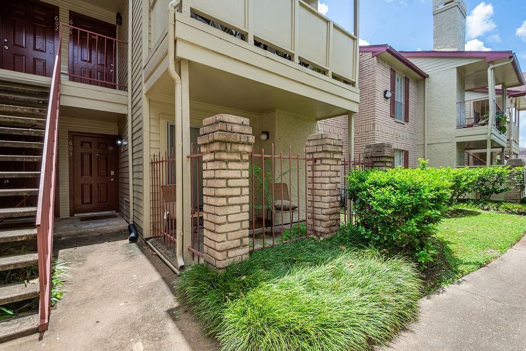 Multi-unit building entrances with red railings, brick columns, an outdoor staircase, and landscaped walkway.