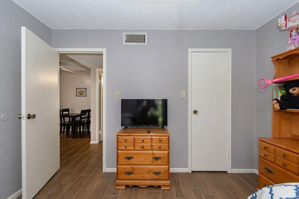 Bedroom with a television on a wooden dresser and an open doorway to the dining area.