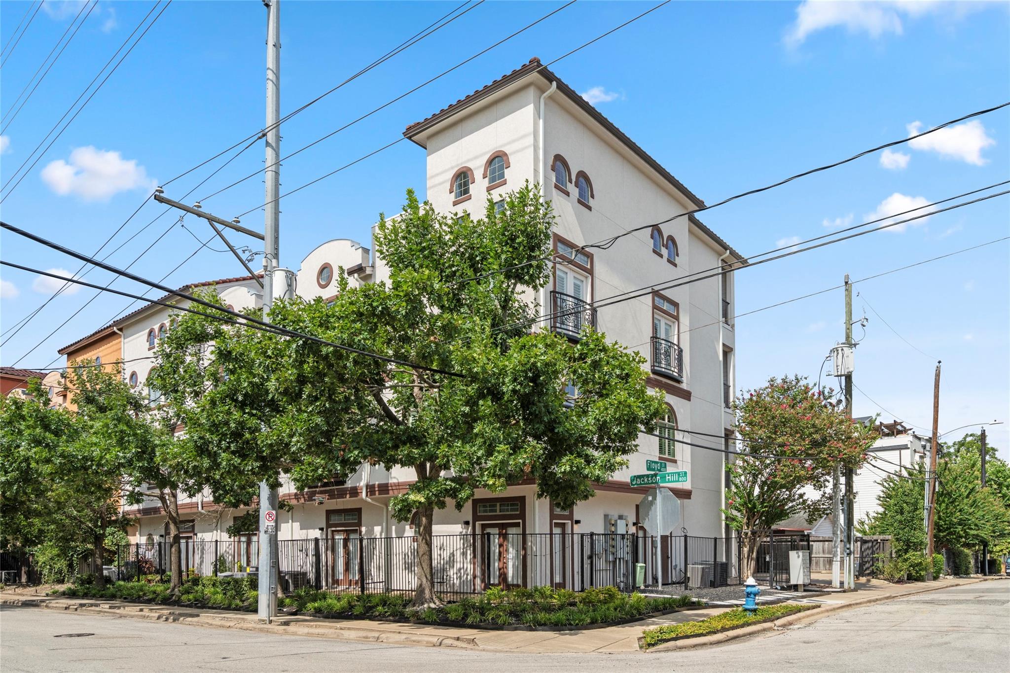 Multi-story stucco residential building with arched windows and balconies at a tree-lined street corner.