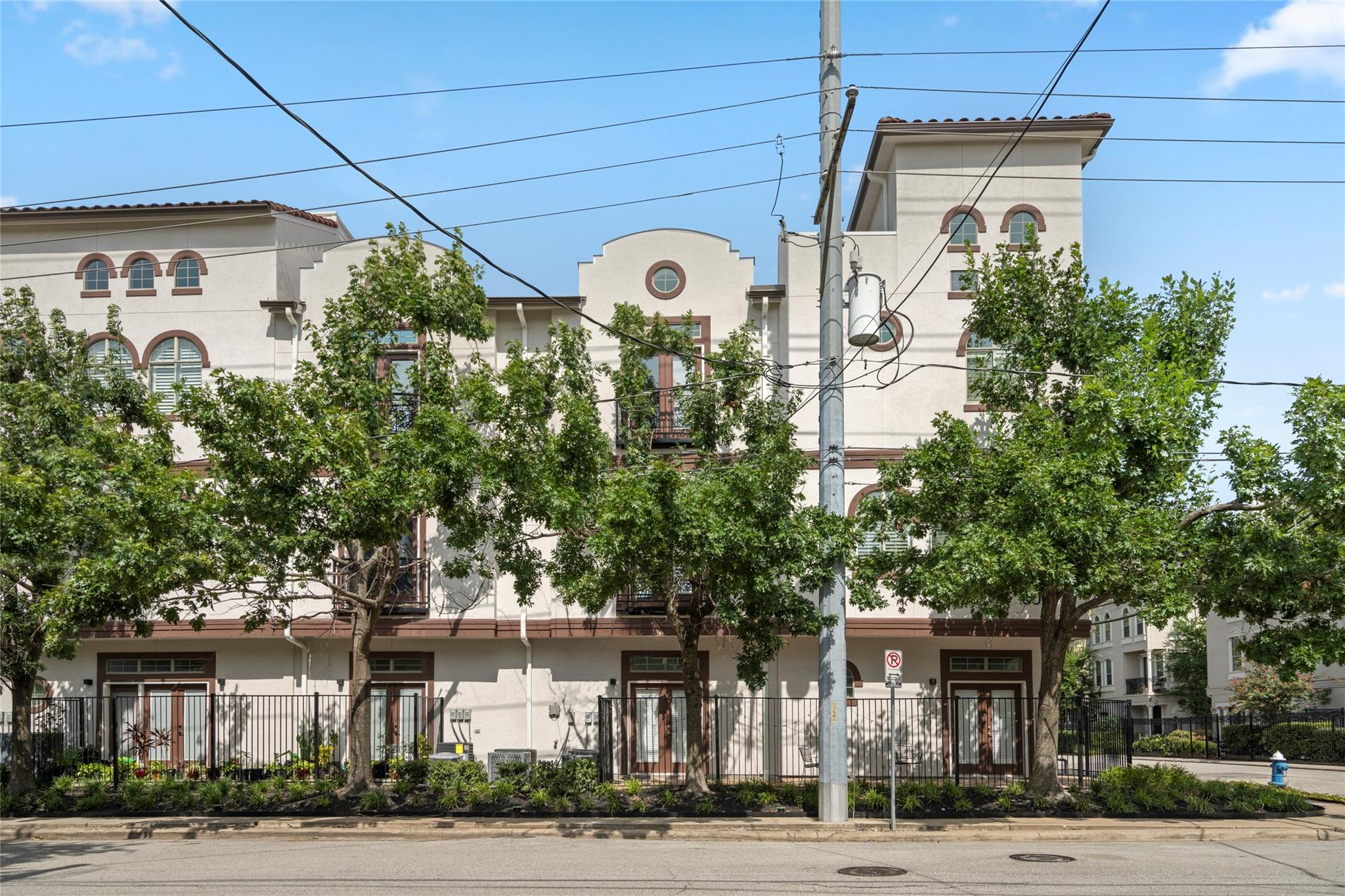Cream-colored residential building with arched windows and balconies behind street trees and overhead wires.