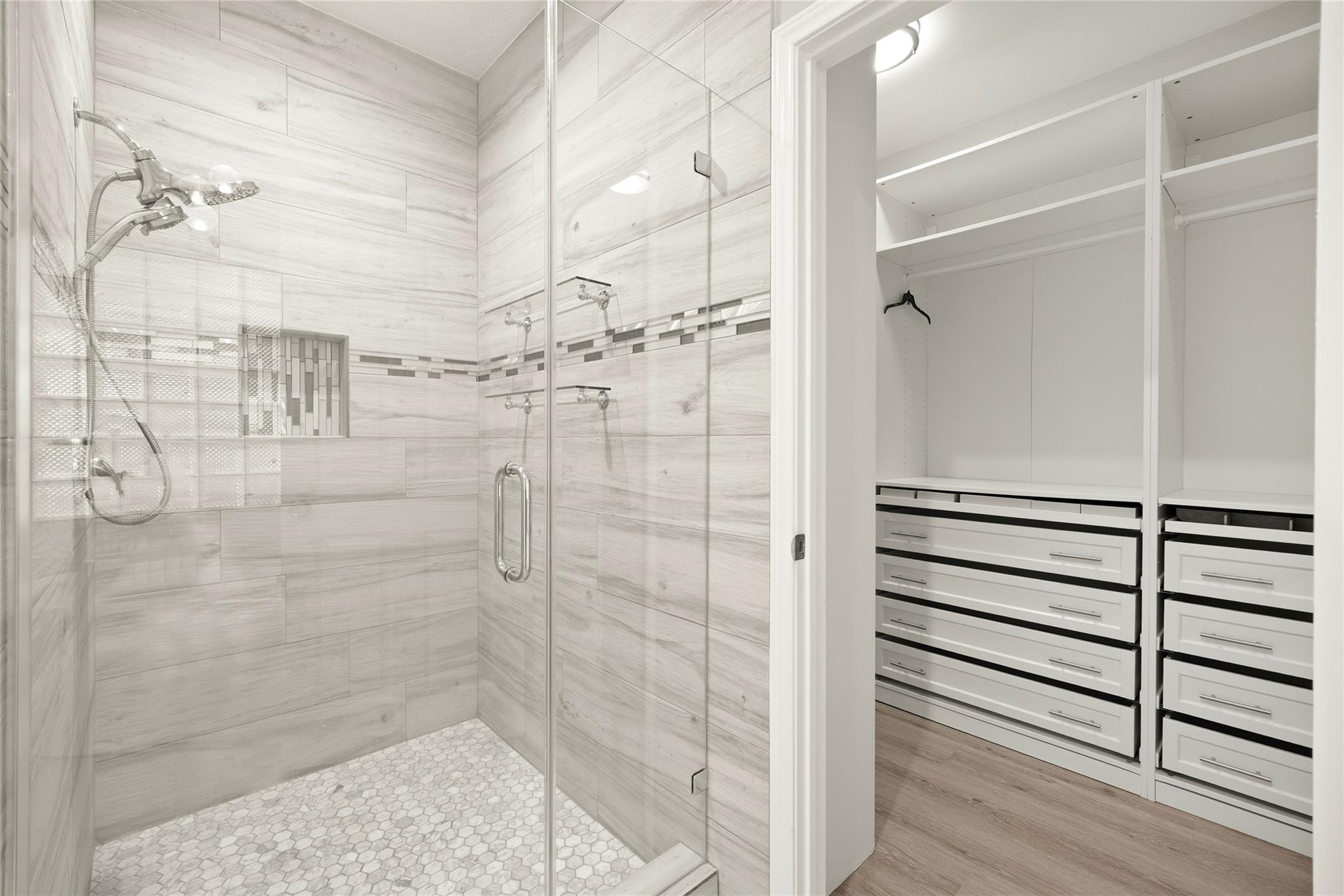 Bathroom with a tiled glass shower beside a walk-in closet with built-in drawers.