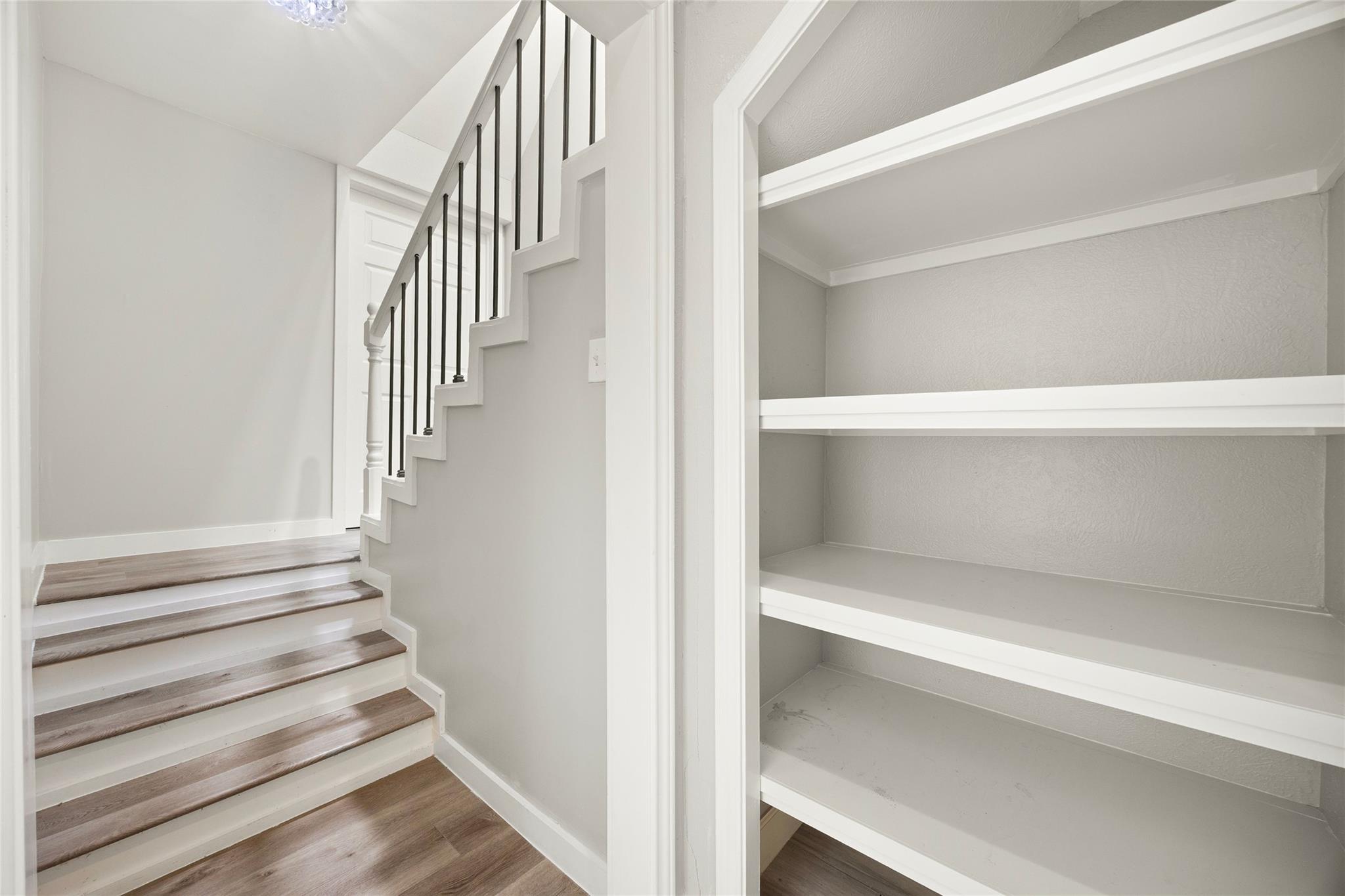 Staircase with wood treads and black balusters beside empty built-in shelves.