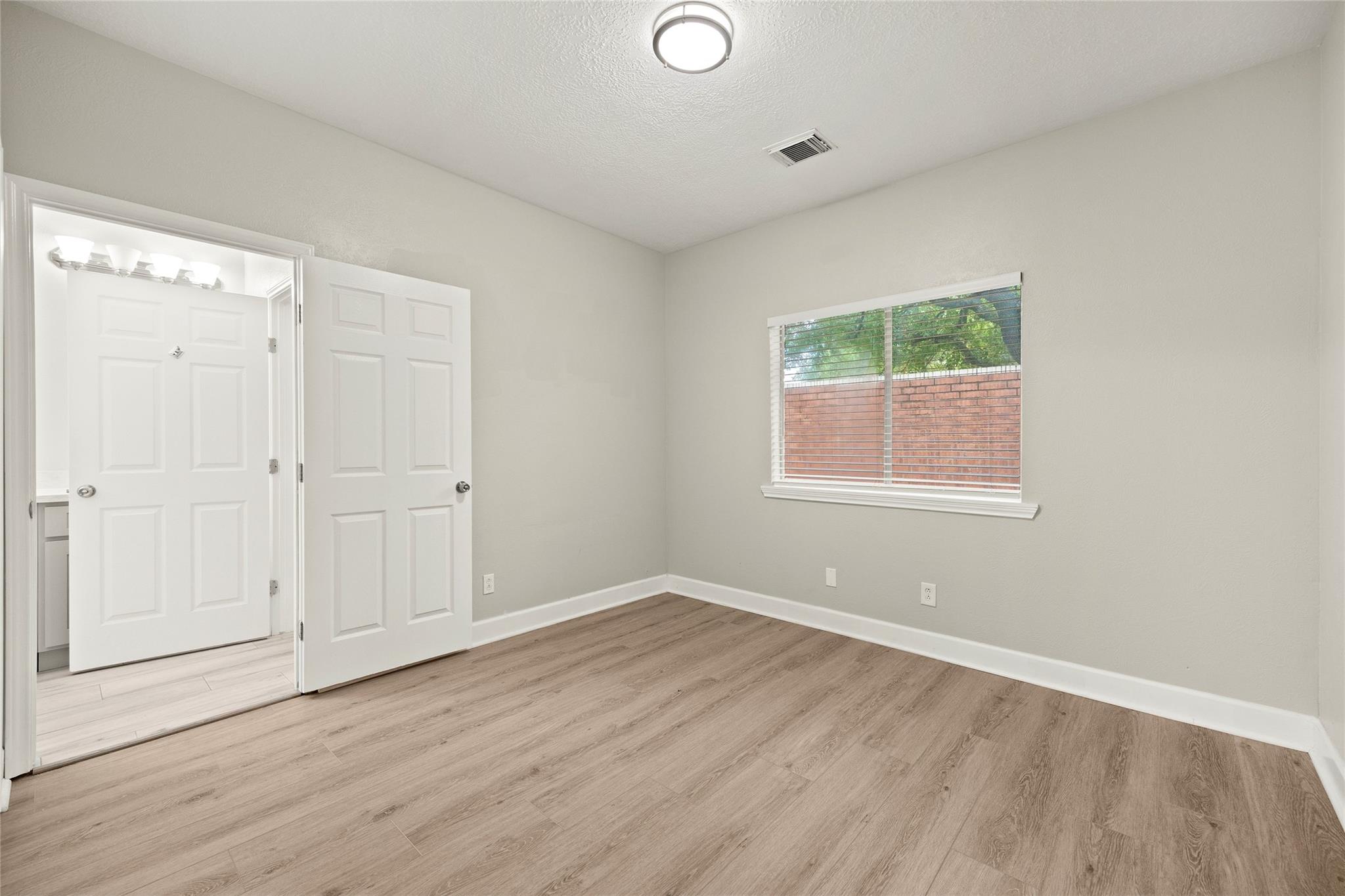 Vacant bedroom with wood-look flooring, a window, and an open doorway to the bathroom.