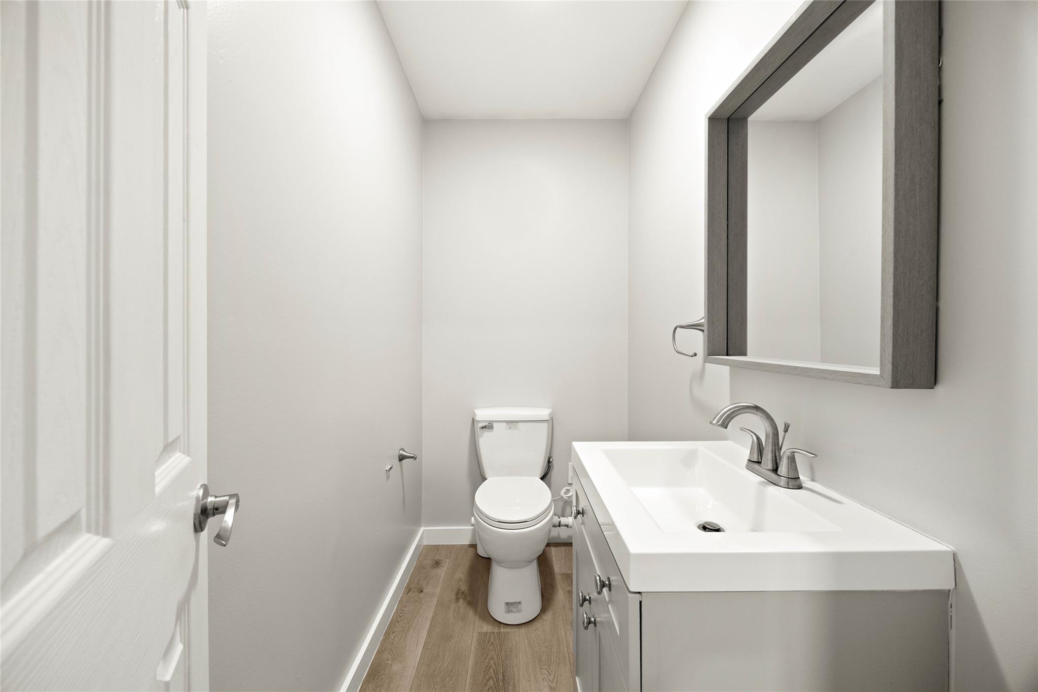 Bathroom with a white toilet, rectangular vanity sink, dark-framed mirror, and wood-look floor.