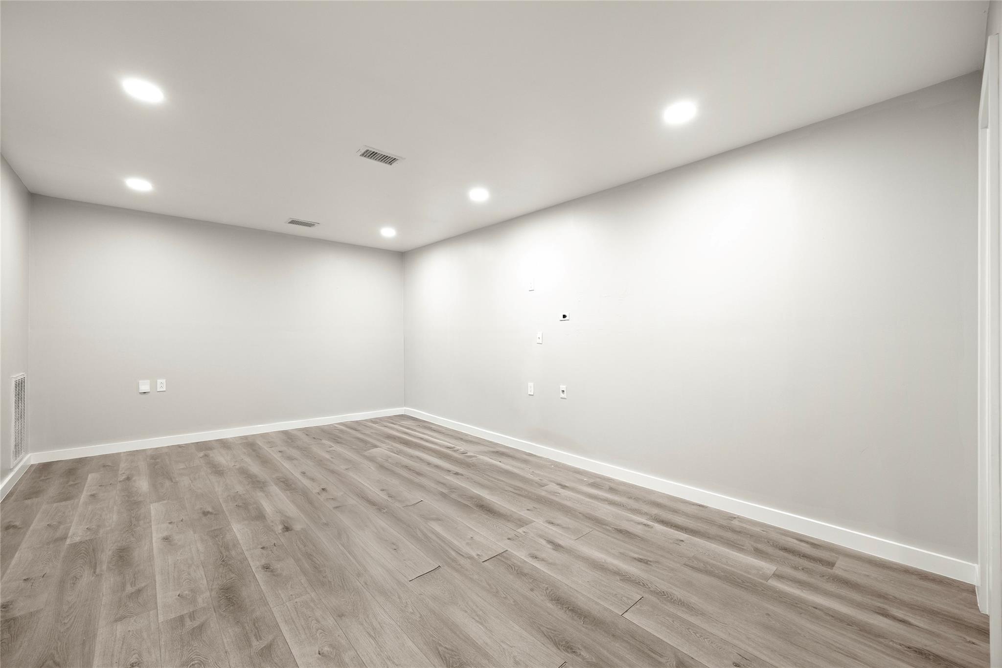 Empty room with wood-look plank flooring and recessed ceiling lights.