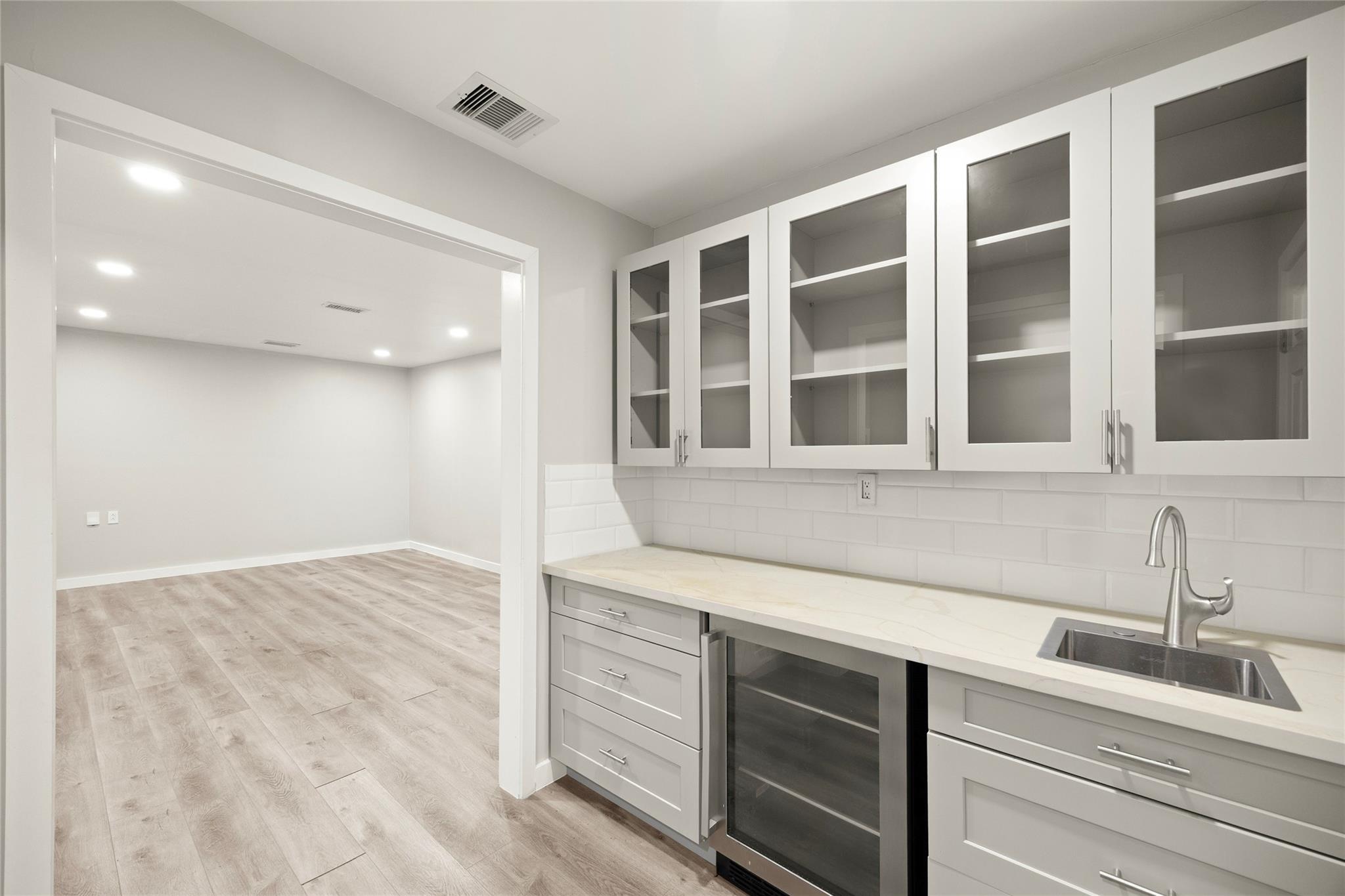 Built-in wet bar with glass-front cabinets and stainless sink opening onto an empty room.
