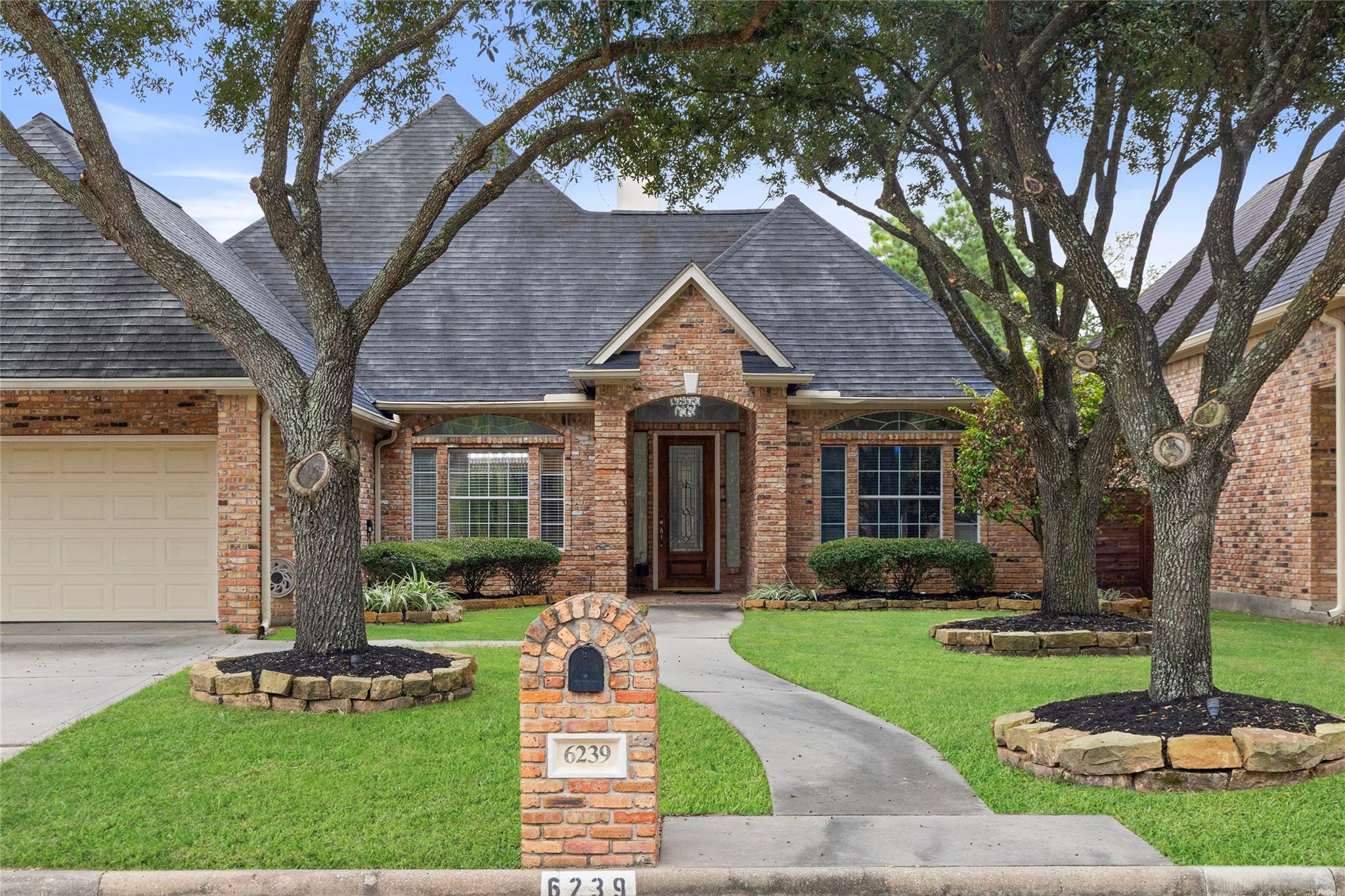 Brick home with a gray shingle roof, mature trees, and a curved front walkway; mailbox marked 6239.