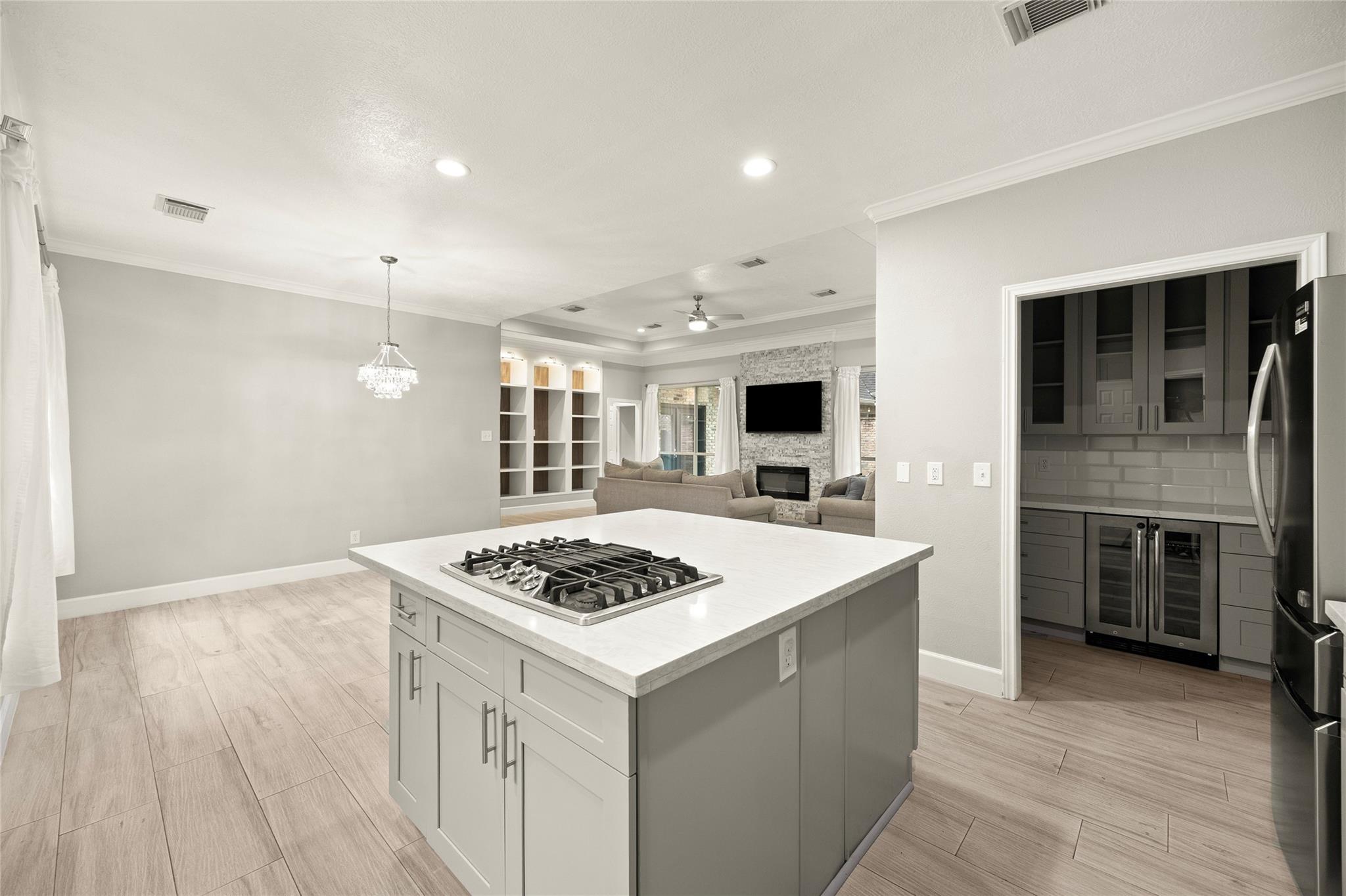 Open kitchen with a white cooktop island, dark cabinetry, and living area with a stone fireplace.