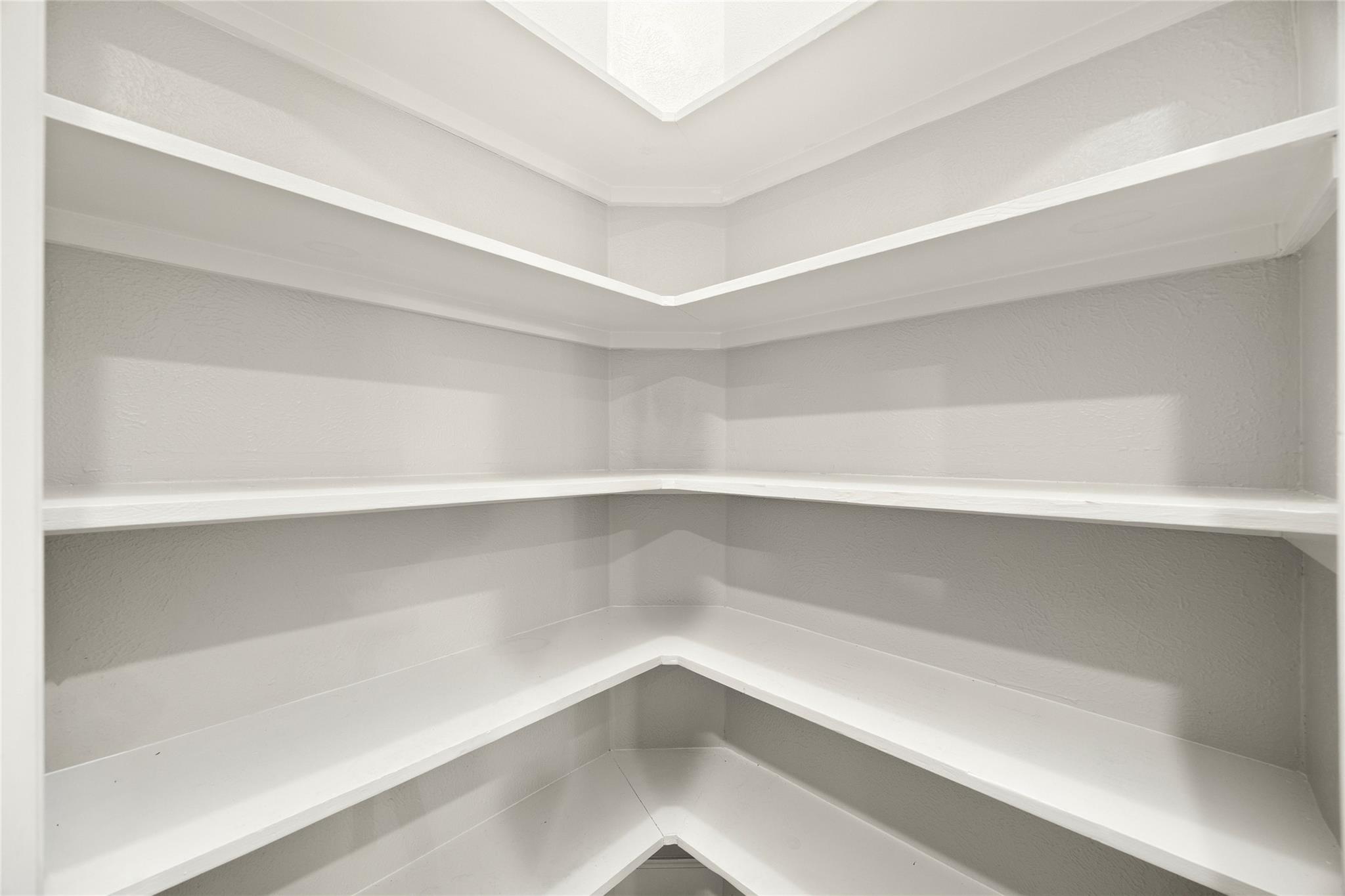 Walk-in pantry with white wraparound shelves and corner shelving.