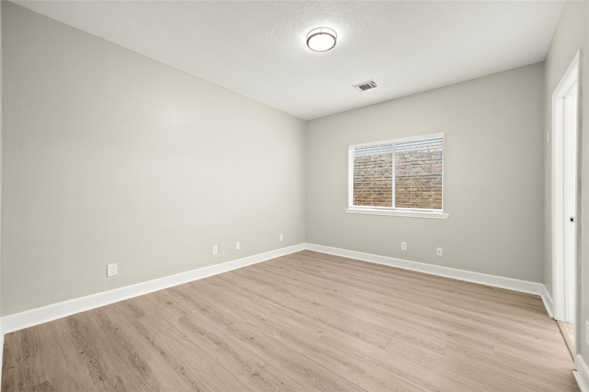 Vacant room with light wood-look floors, a window with blinds, and a ceiling light.