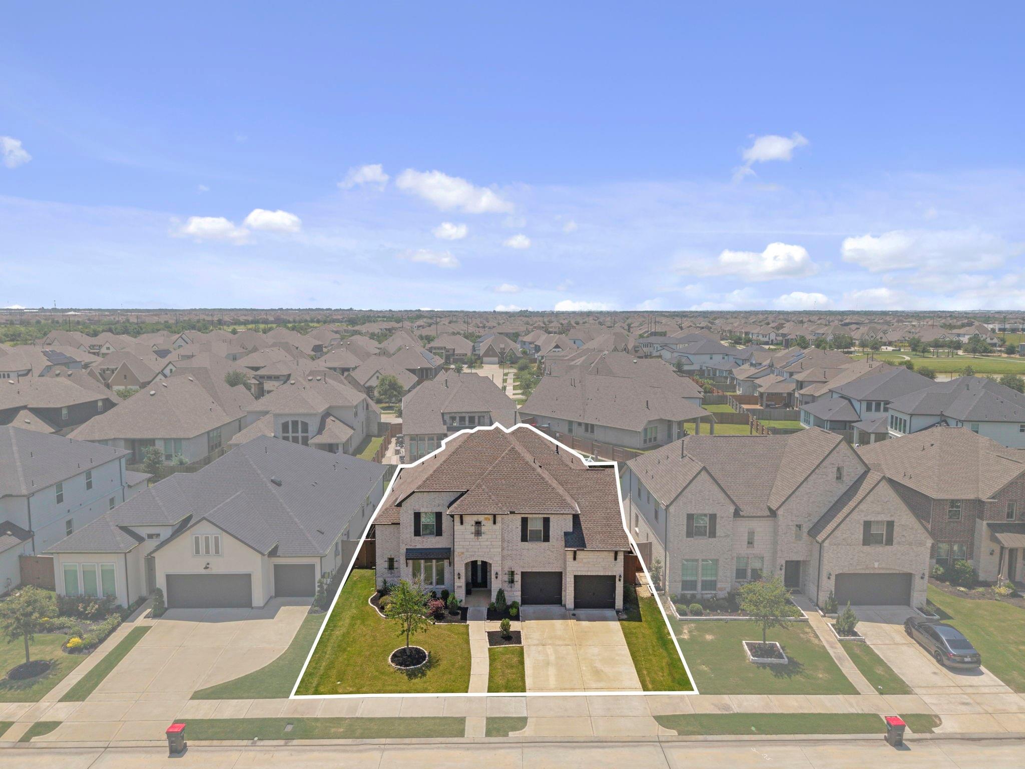 Aerial view of a two-story brick house with a landscaped lawn and double garage.
