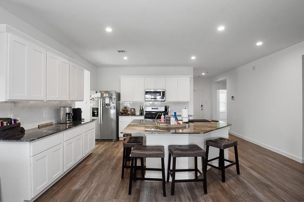 Open kitchen with white cabinets, stainless steel appliances, and a large island with stools.