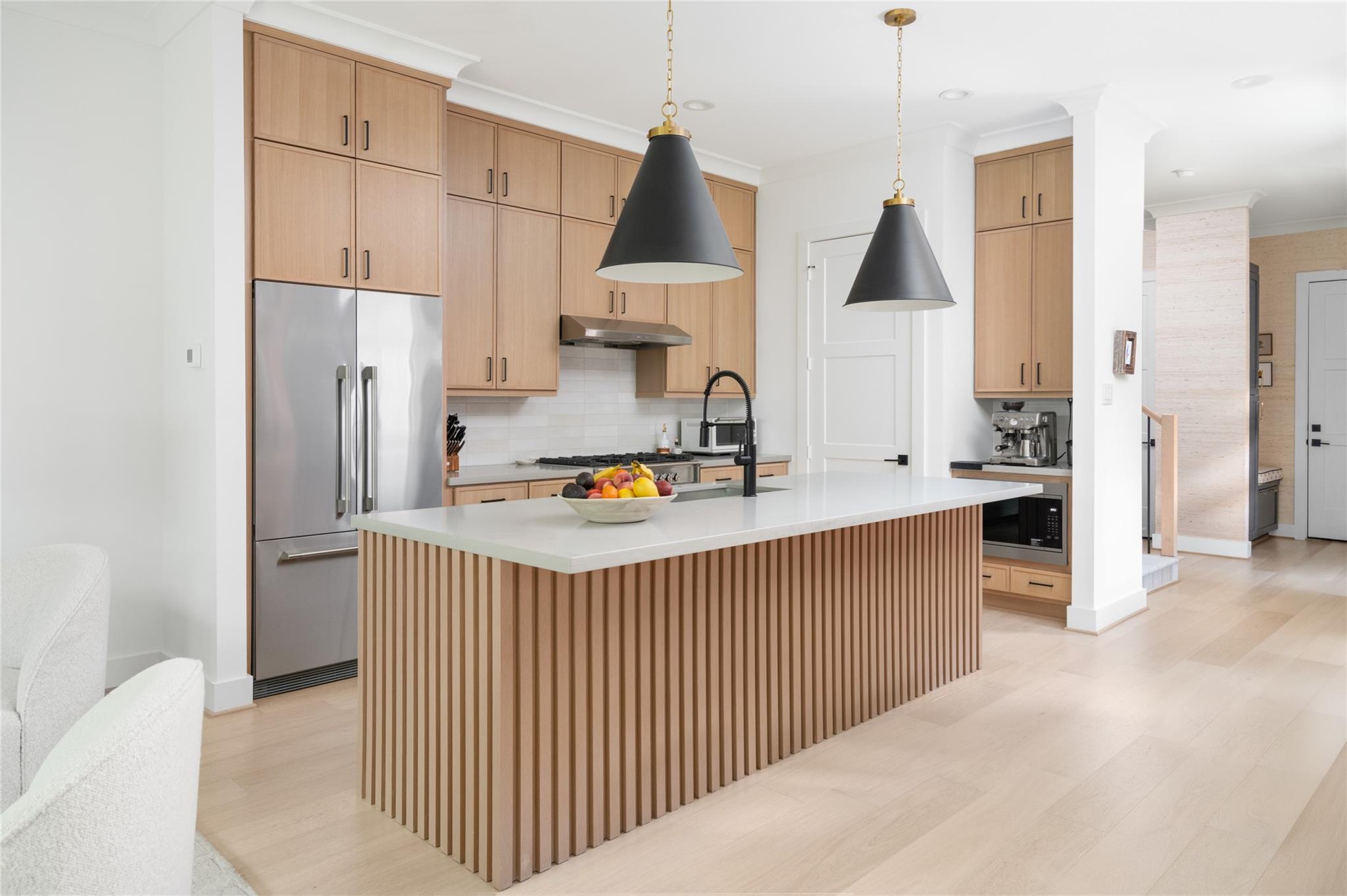 Modern kitchen with light wood cabinets, stainless appliances, and a large fluted island.