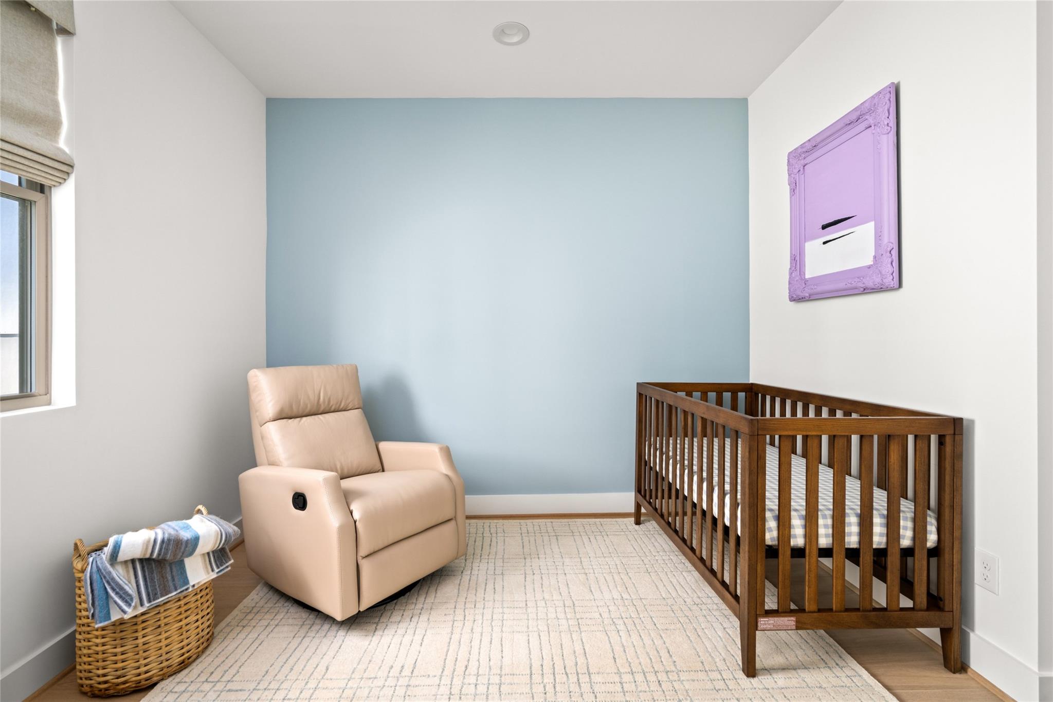 Nursery with a wooden crib, beige recliner, and pale blue accent wall.