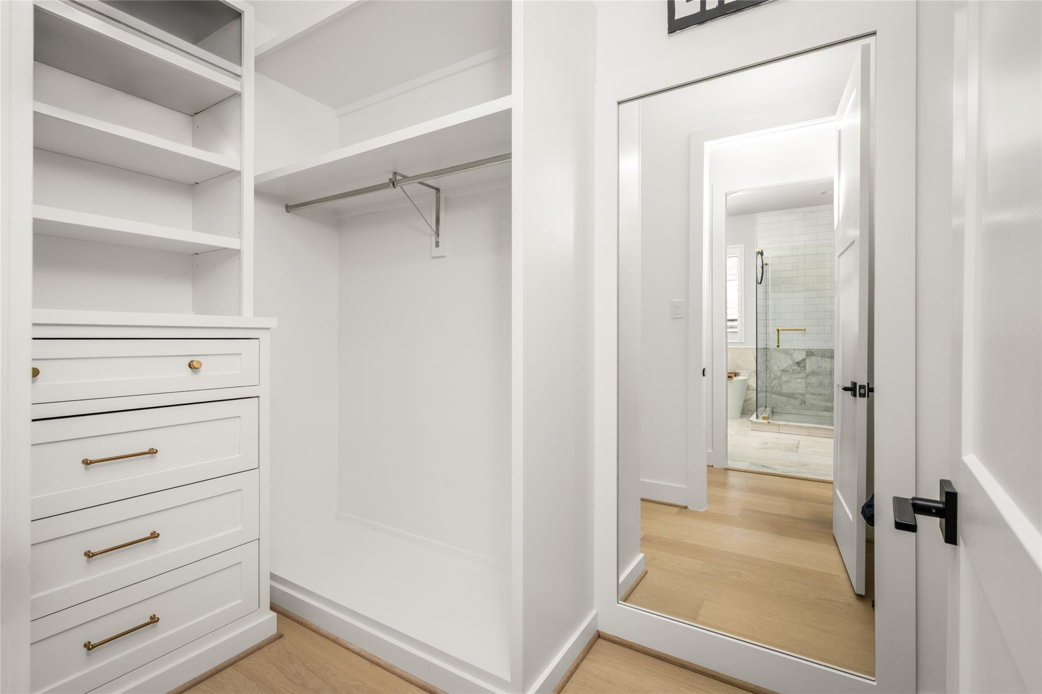Walk-in closet with built-in drawers and shelving, looking through to a tiled walk-in shower.