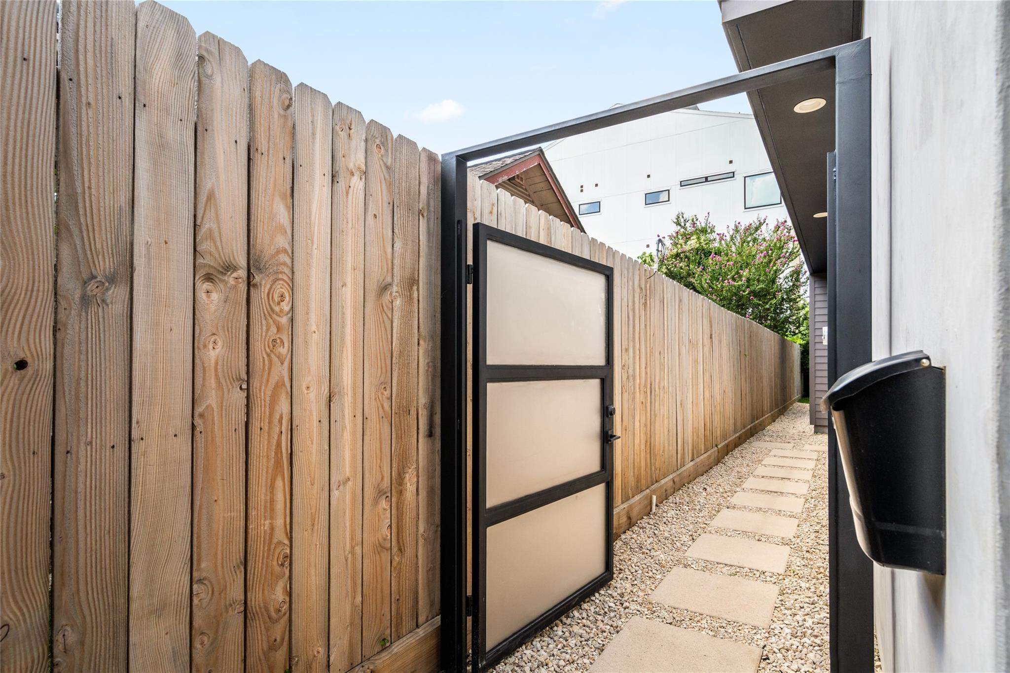 Side yard with an open gate, wooden privacy fence, gravel, and stepping-stone path.