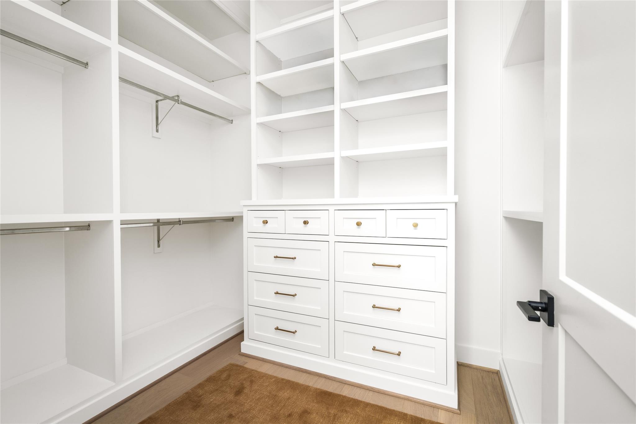 Walk-in closet with white built-in shelves, hanging rods, and brass-hardware drawers.
